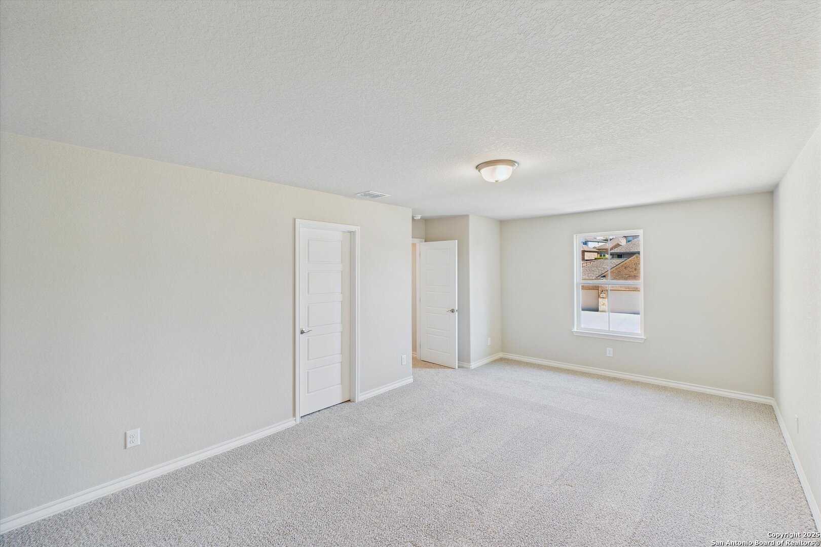 Spacious empty bedroom with beige walls, carpet floor, window, and bath door in Davidson Homes The Jennings H, Ladera, San Antonio