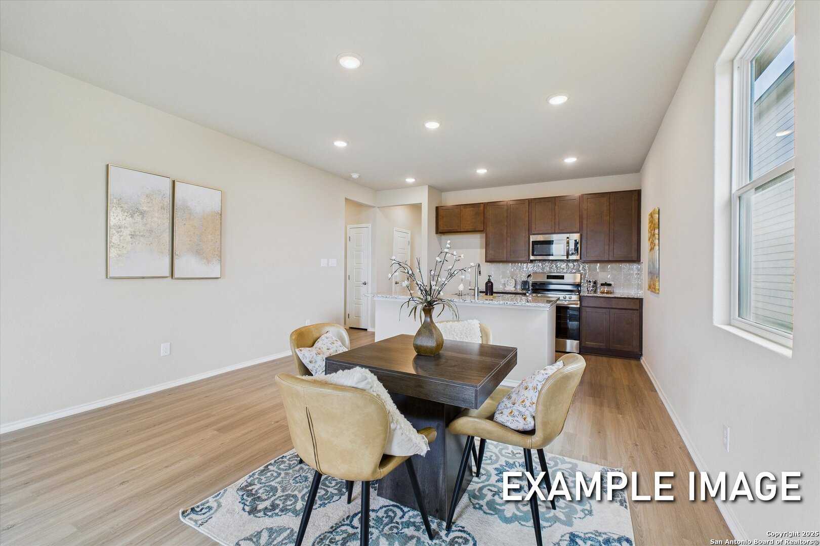 Modern dining area with wooden table, cushioned chairs, and rug adjacent to kitchen in Davidson Homes The Comal B, Agave, San Antonio