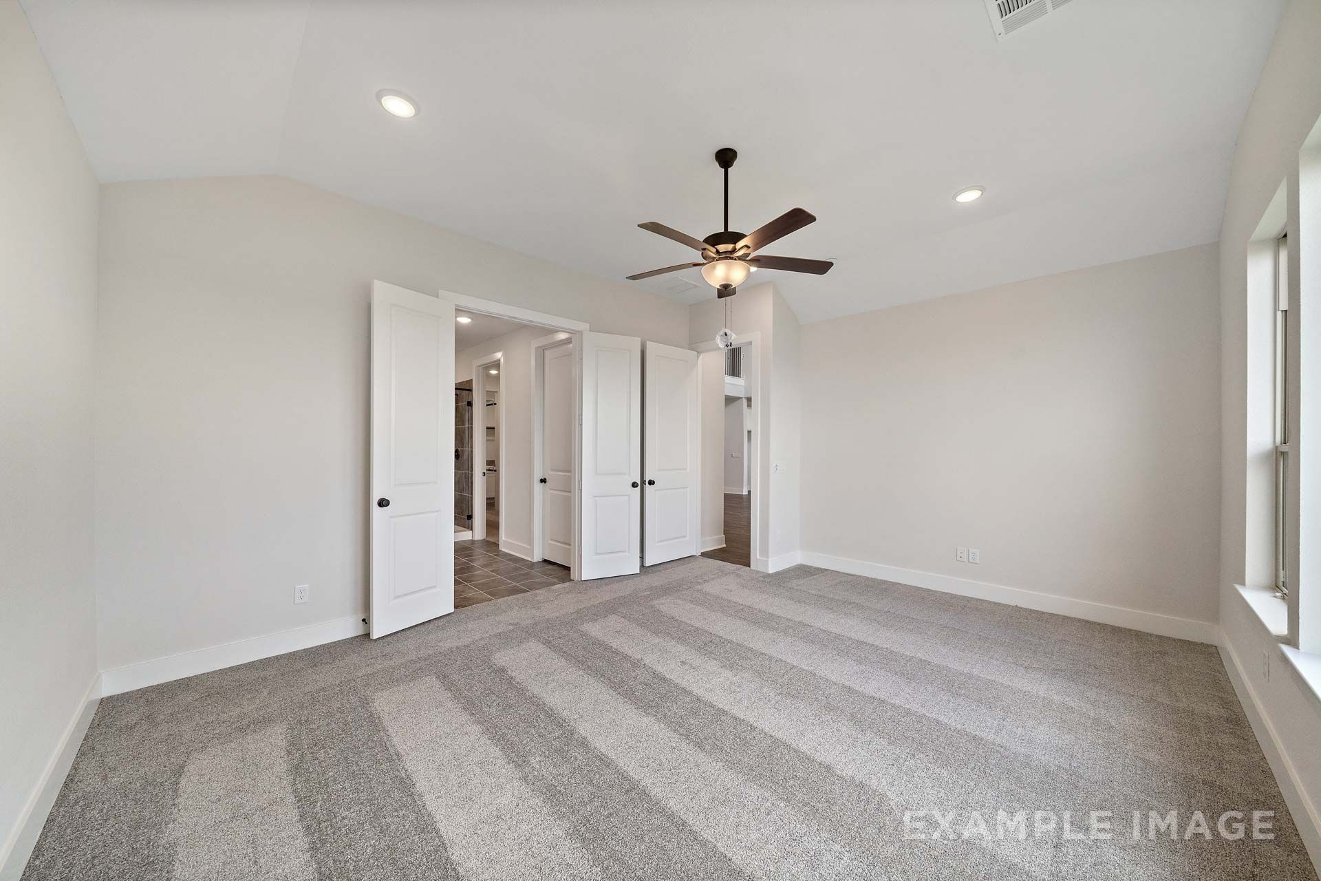 Spacious master suite on main floor of The Victoria by Davidson Homes with vaulted ceiling, ceiling fan, and en suite bath access.