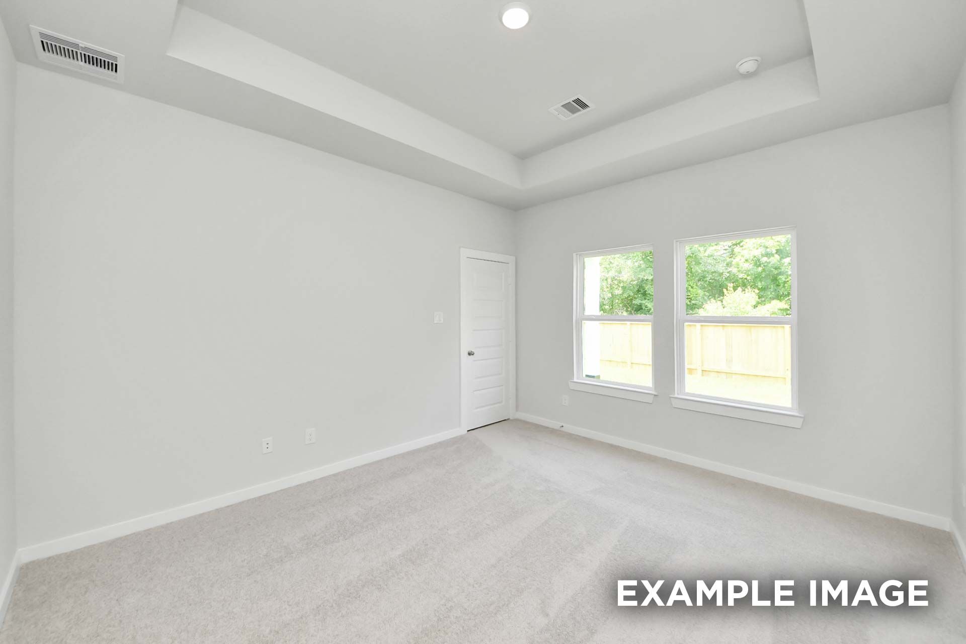 Spacious master suite in The Blanco by Davidson Homes featuring tray ceiling, carpet flooring, and large windows overlooking backyard.