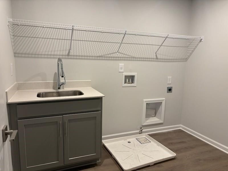 Modern laundry room with gray cabinets, utility sink, wire shelving, and washer/dryer hookups in Davidson Homes The Marion A, Winder, Georgia