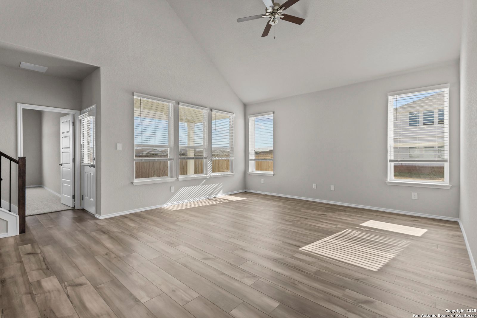 Bright living room with vaulted ceiling, ceiling fan, large windows, and hardwood floors in The Collin B, Seguin, Texas