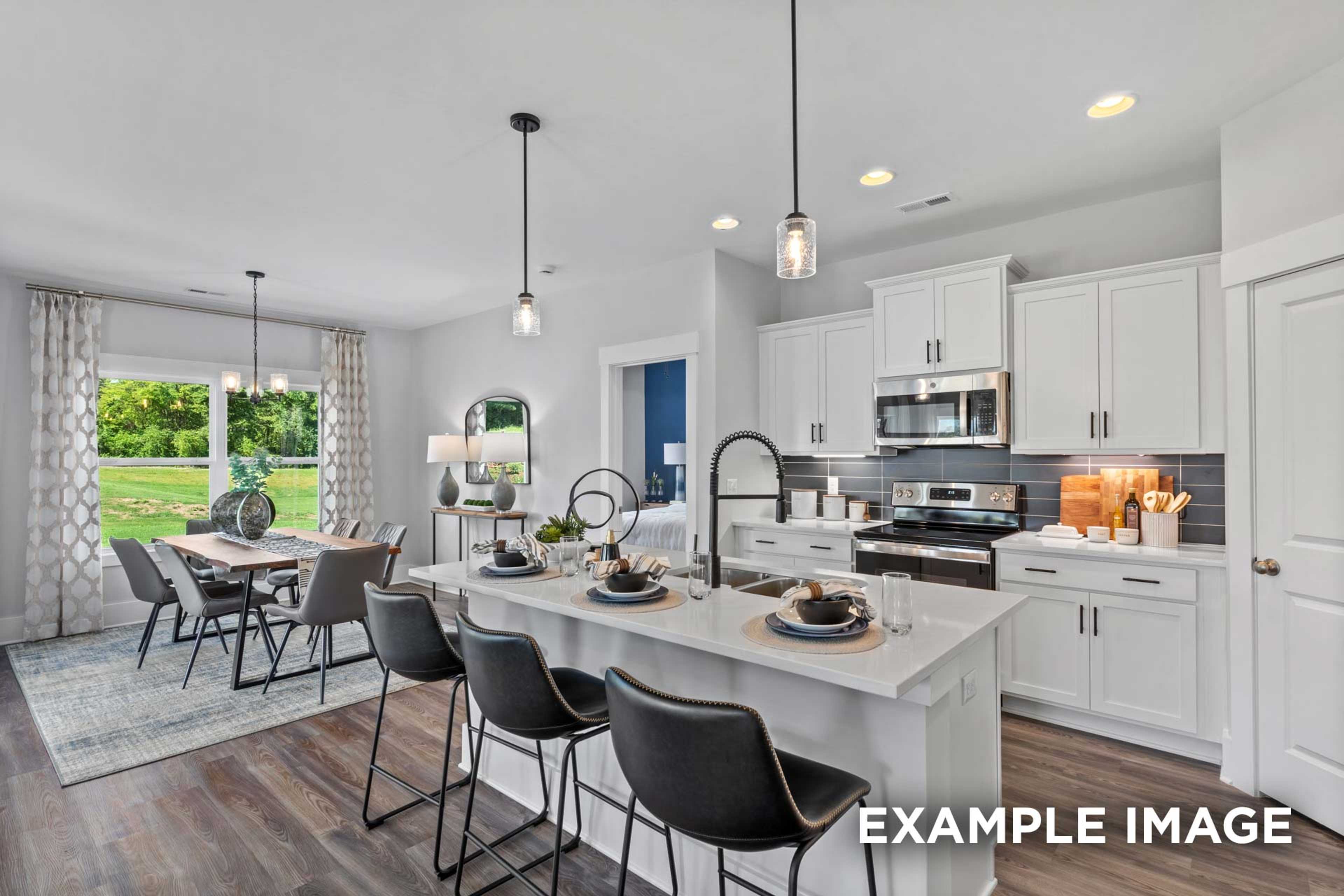 Spacious open-concept kitchen and dining in The Franklin C with white shaker cabinets, large island, bar stools, and window views