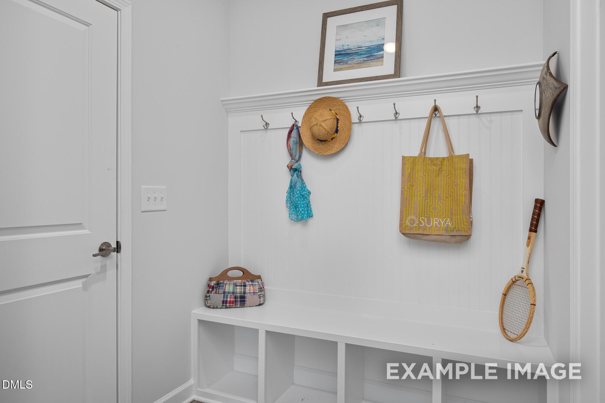 Cozy mudroom with white bench, wall hooks holding sun hat, scarf, SURA beach bag, tennis racket in Davidson Homes The Cypress B II, Angier, NC