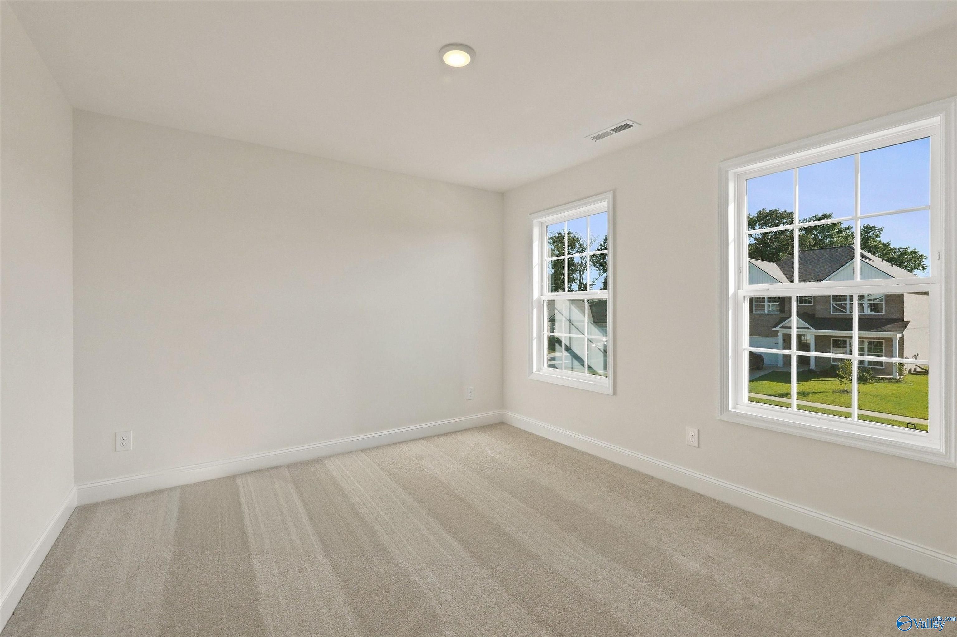 Bright bedroom with neutral carpet and large windows in The Chelsea C floor plan at Creek Grove, New Market, Alabama.