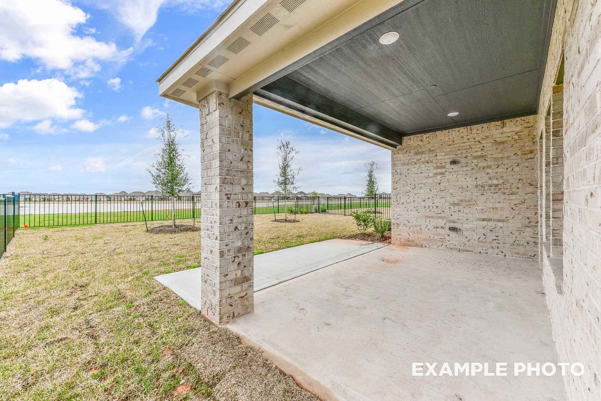 Covered back patio with black ceiling, recessed lights, and stone columns overlooking grassy yard in Davidson Homes The Riviera A, Rosharon, Texas