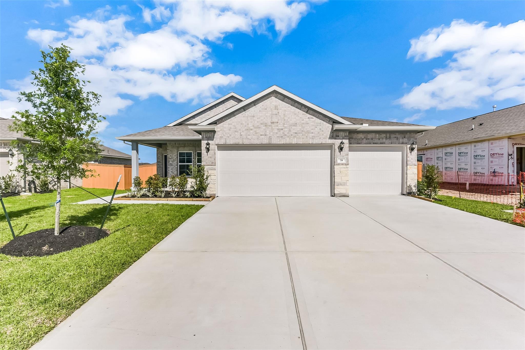 Modern beige brick single-story home with 3-car garage, concrete driveway, and landscaped yard in River Ranch Meadows, Dayton, Texas