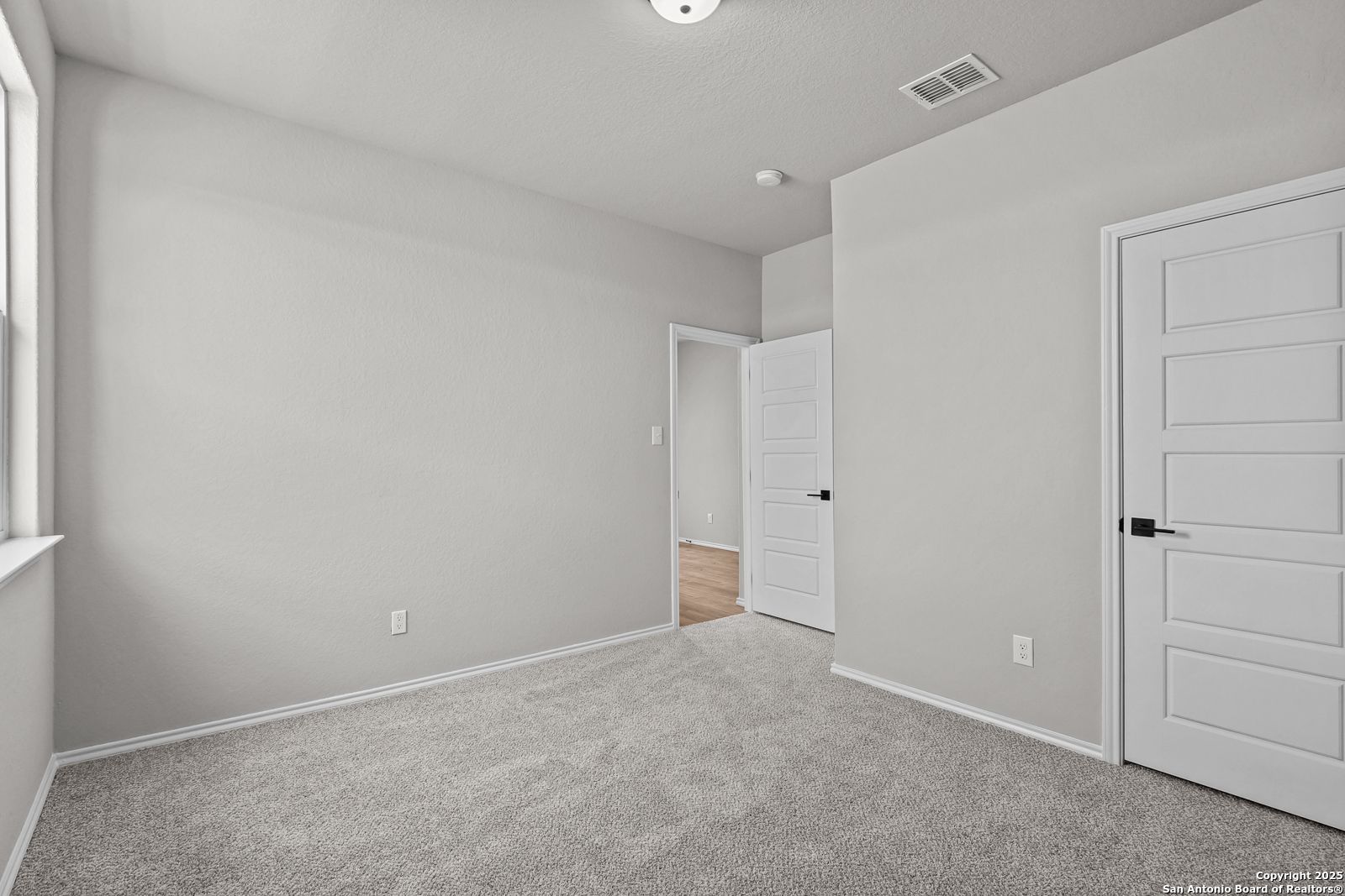 Empty secondary bedroom featuring light gray walls, white paneled doors, beige carpet, and large window in Davidson Homes The Daphne K, San Antonio