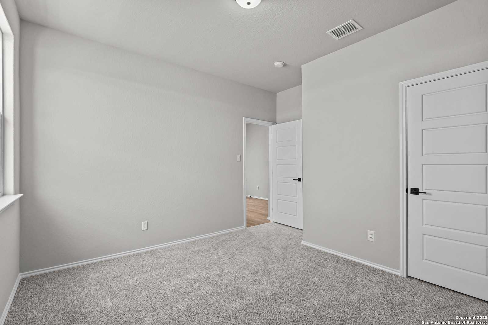 Spacious empty bedroom with gray walls, carpet flooring, and white doors in Davidson Homes The Daphne K, San Antonio