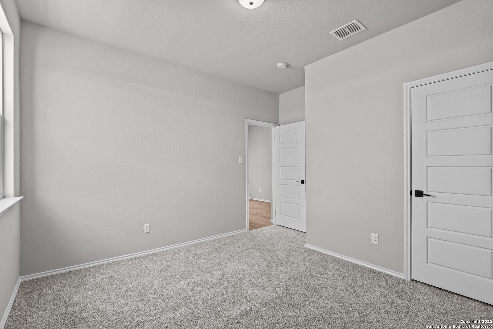 Empty secondary bedroom featuring light gray walls, white paneled doors, beige carpet, and large window in Davidson Homes The Daphne K, San Antonio