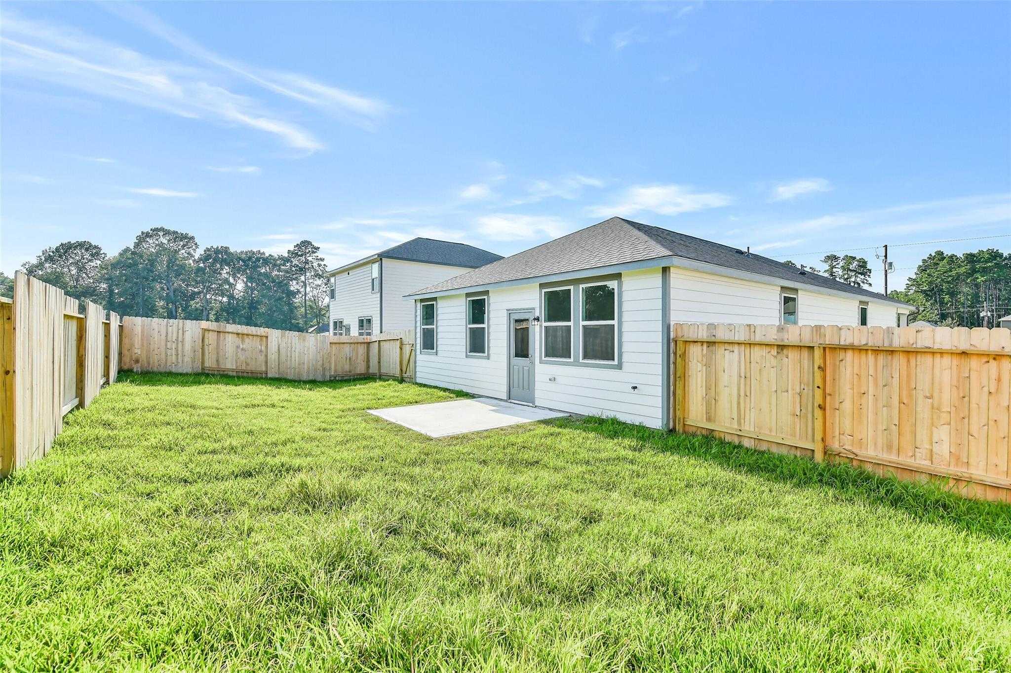 Side view of white single-story 4-bedroom home with fenced backyard, lush green lawn, and pine trees in Liberty Estates, Cleveland, Texas