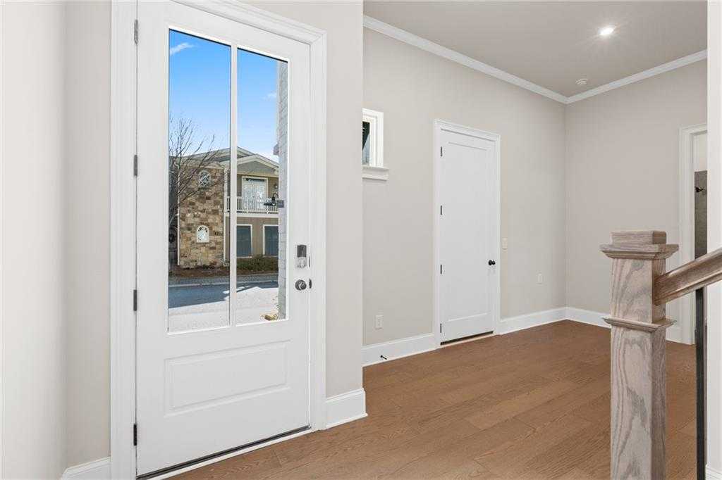 Bright entry foyer with glass-paneled front door, hardwood floors, and wooden staircase in Davidson Homes The Seaside A, Woodstock, Georgia