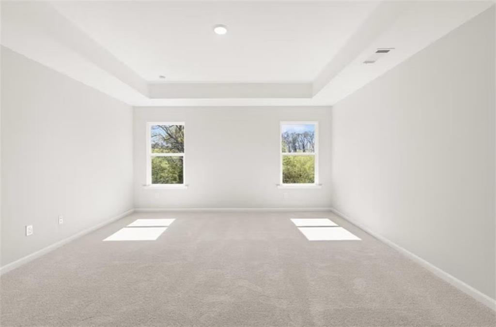 Spacious empty bedroom featuring light gray walls, gray carpet, large windows with tree views, and tray ceiling in The Hickory B, Winder, GA