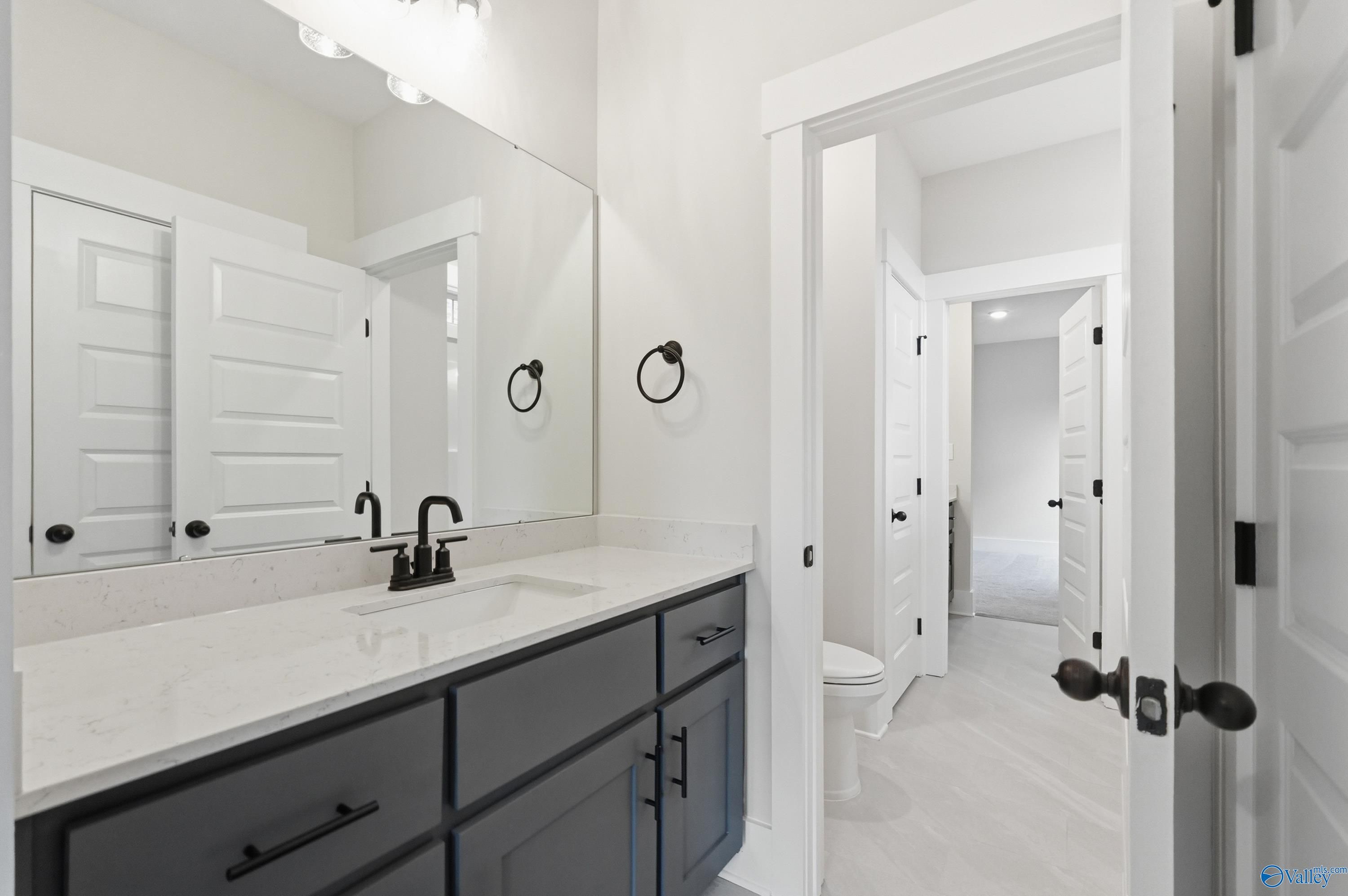 Modern master bathroom with dark vanity, white quartz countertop, large mirror, and open door in Davidson Homes The Finleigh, Meridianville AL