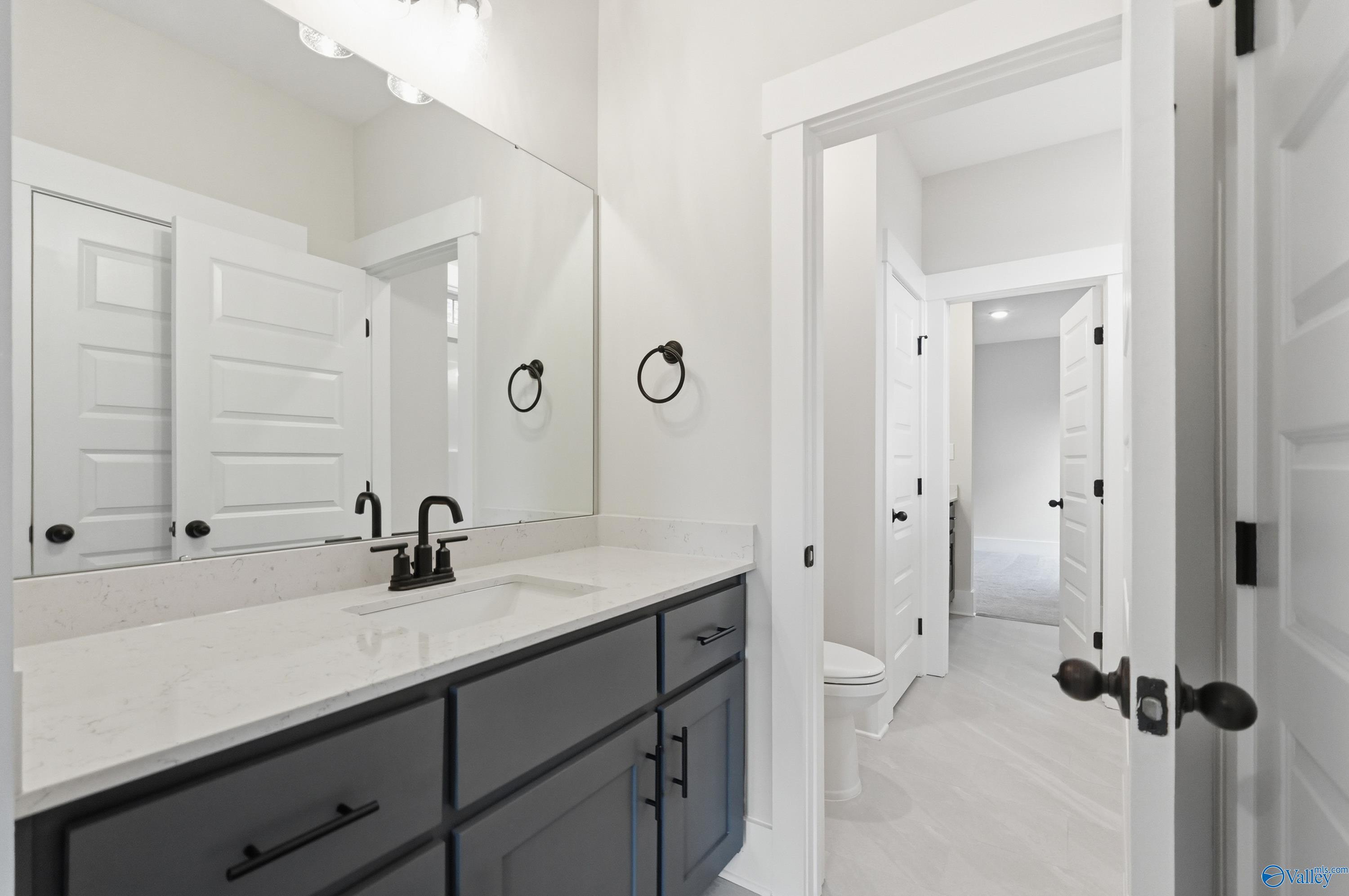 Modern master bathroom with dark vanity, white quartz countertop, large mirror, and open door in Davidson Homes The Finleigh, Meridianville AL