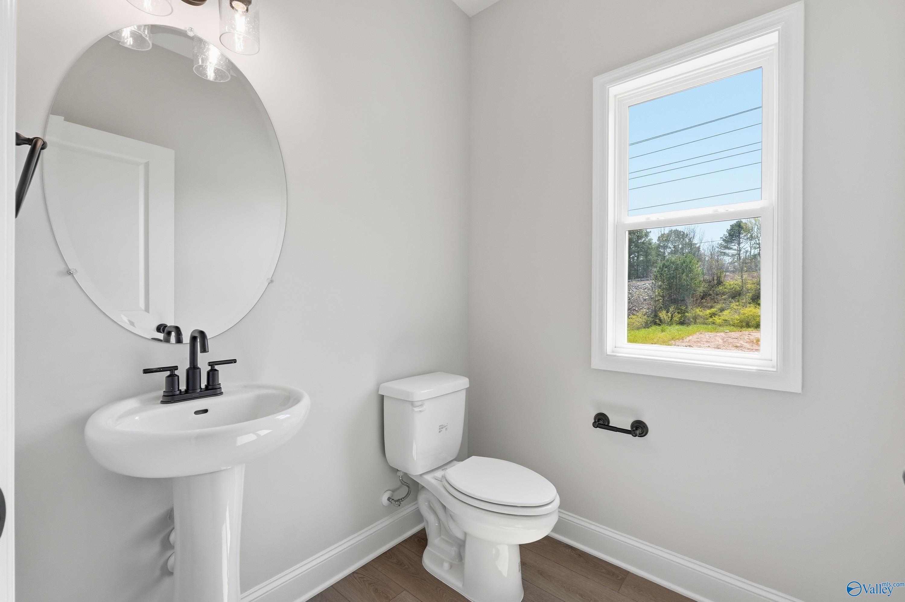 Elegant powder room featuring white pedestal sink, round mirror, and window view in Davidson Homes The Chelsea D, Cullman Alabama