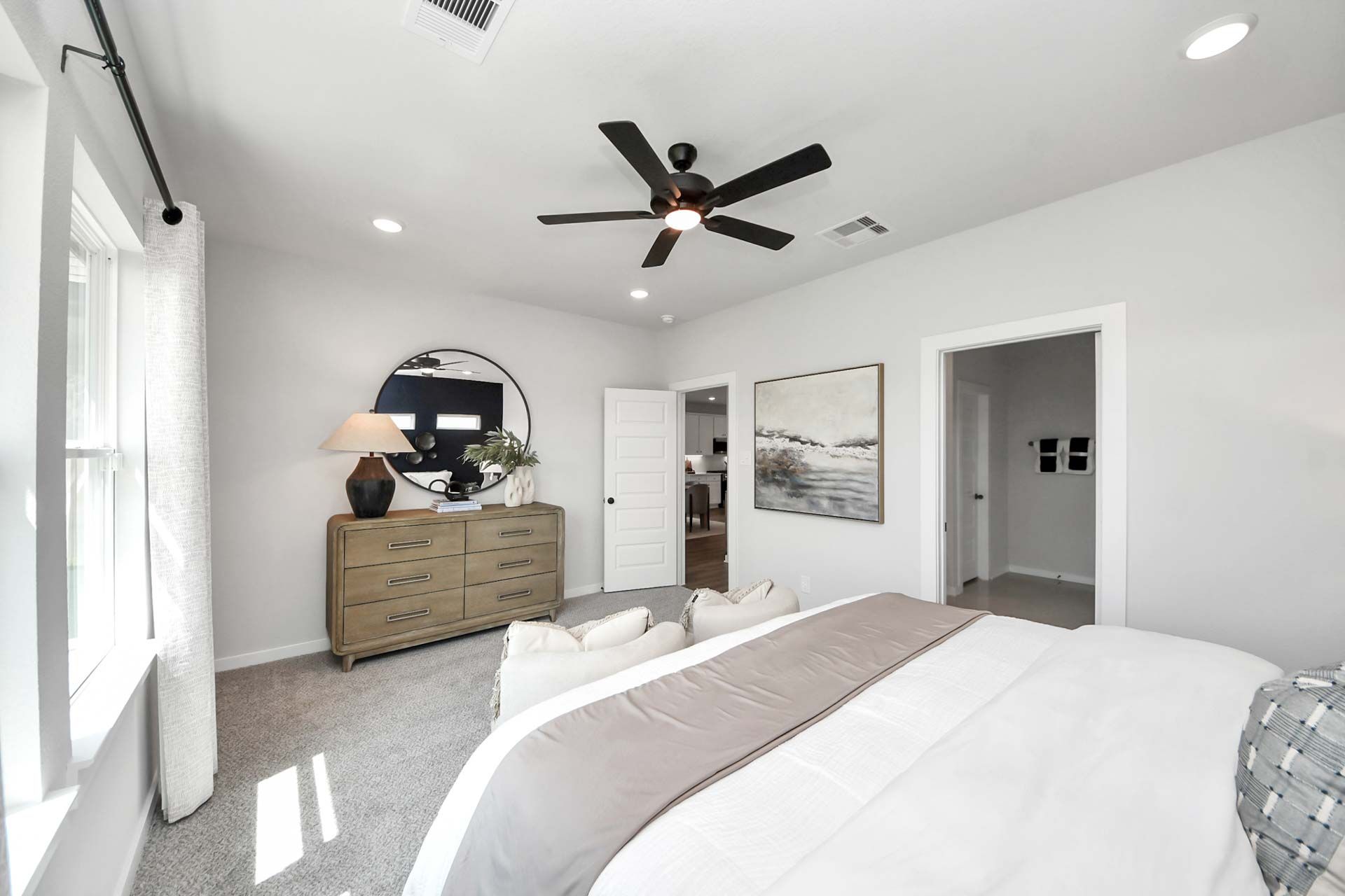 Spacious primary bedroom at Enclave at Newport in Crosby, TX, featuring neutral decor, a wooden dresser, and modern lighting.