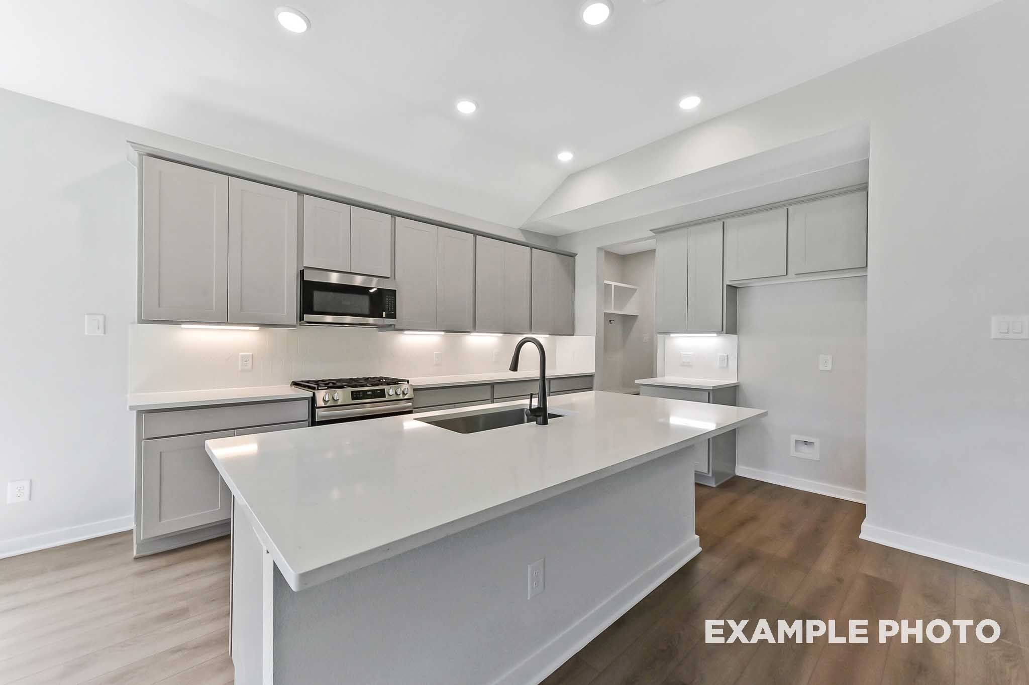 Modern kitchen in The Sequoia with white shaker cabinets, large quartz island, gas range, and hardwood floors