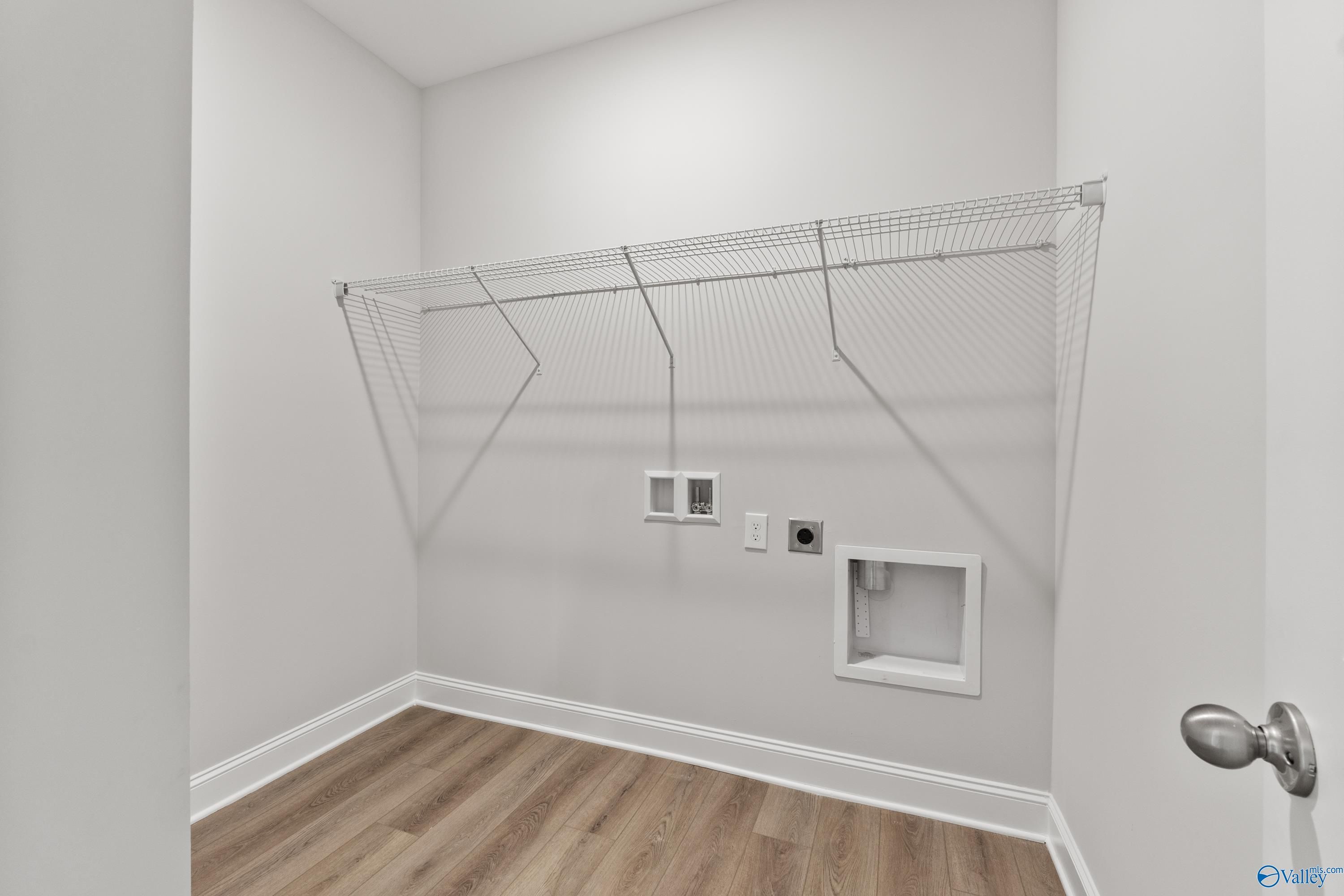 Spacious laundry room with wire shelving, utility sink, outlets, and hardwood floors in Davidson Homes The Daphne, Hazel Green, Alabama