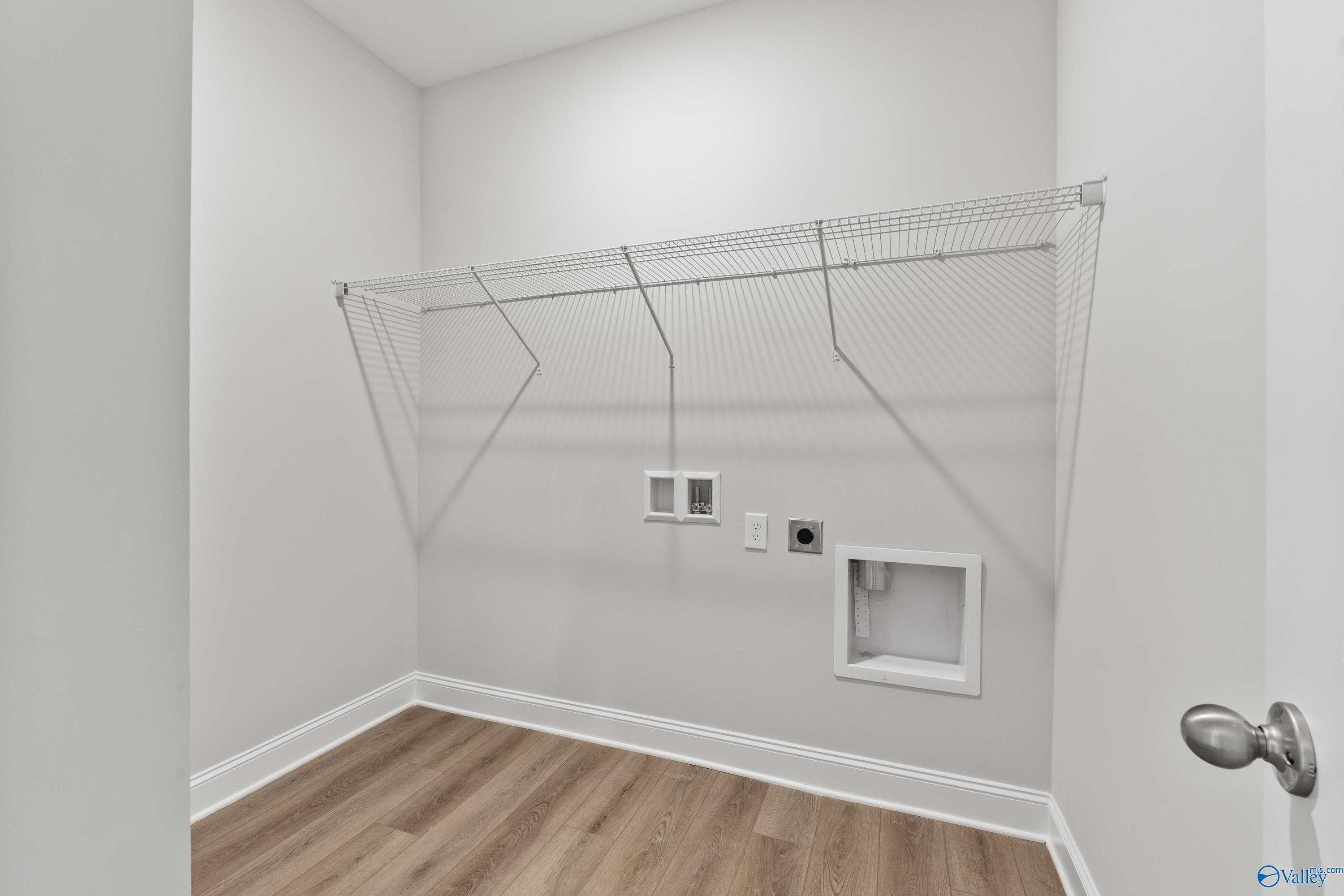 Spacious laundry room with wire shelving, utility sink, outlets, and hardwood floors in Davidson Homes The Daphne, Hazel Green, Alabama