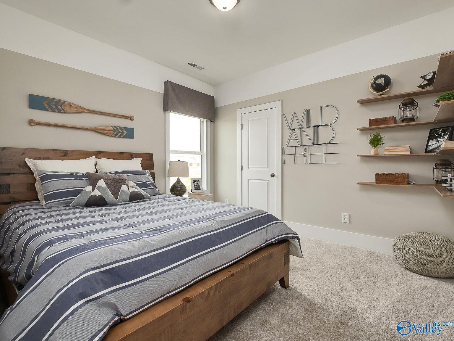 Cozy secondary bedroom with navy striped bedding, wooden frame bed, nautical oar decor, and "Wild and Free" shelves in Davidson Homes The Everett, Toney, Alabama