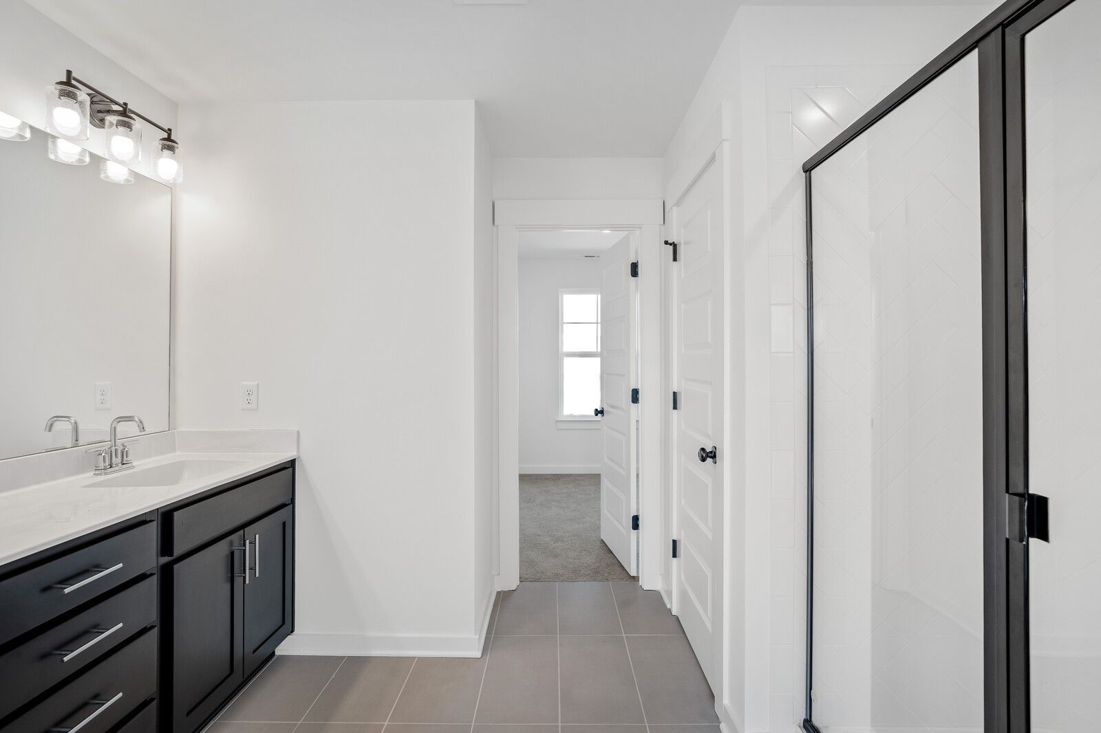 Modern master bathroom featuring double white quartz vanity, dark shaker cabinets, and frameless glass shower in Davidson Homes Willow C, Gallatin, TN