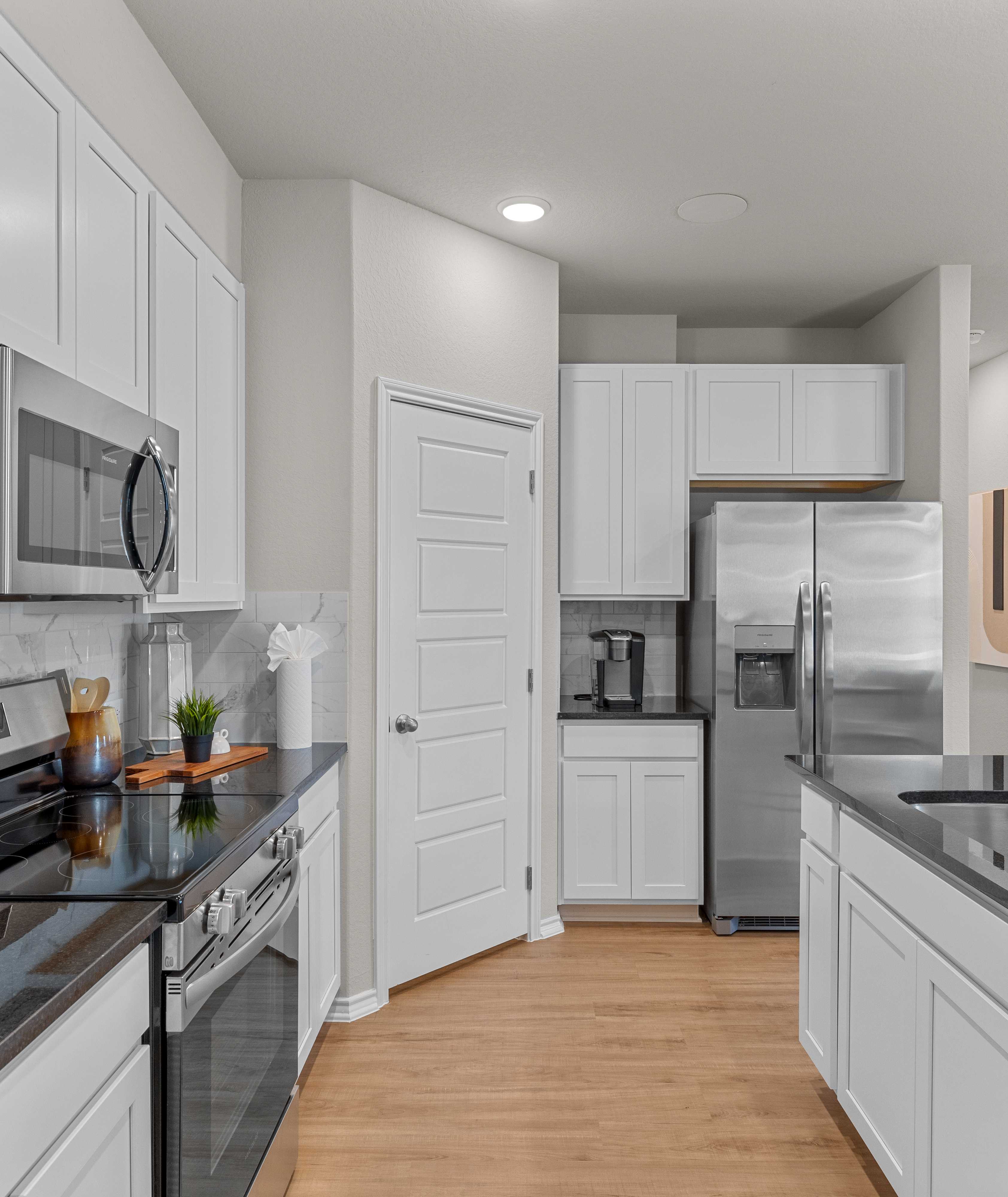 Modern kitchen in Applewhite Meadows San Antonio TX with white shaker cabinets, stainless steel appliances, black quartz counters, hardwood floors