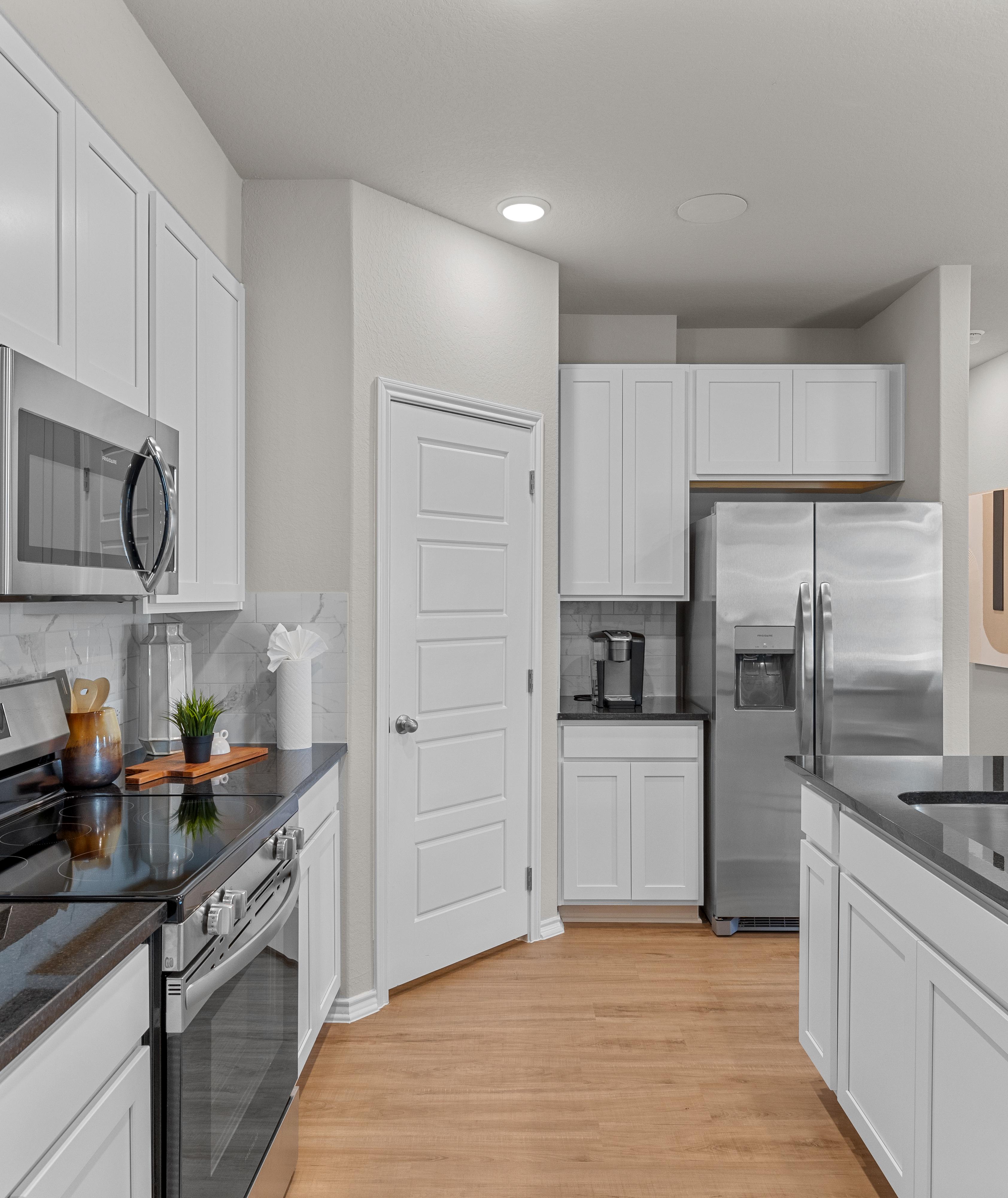 Modern kitchen in Applewhite Meadows San Antonio TX with white shaker cabinets, stainless steel appliances, black quartz counters, hardwood floors