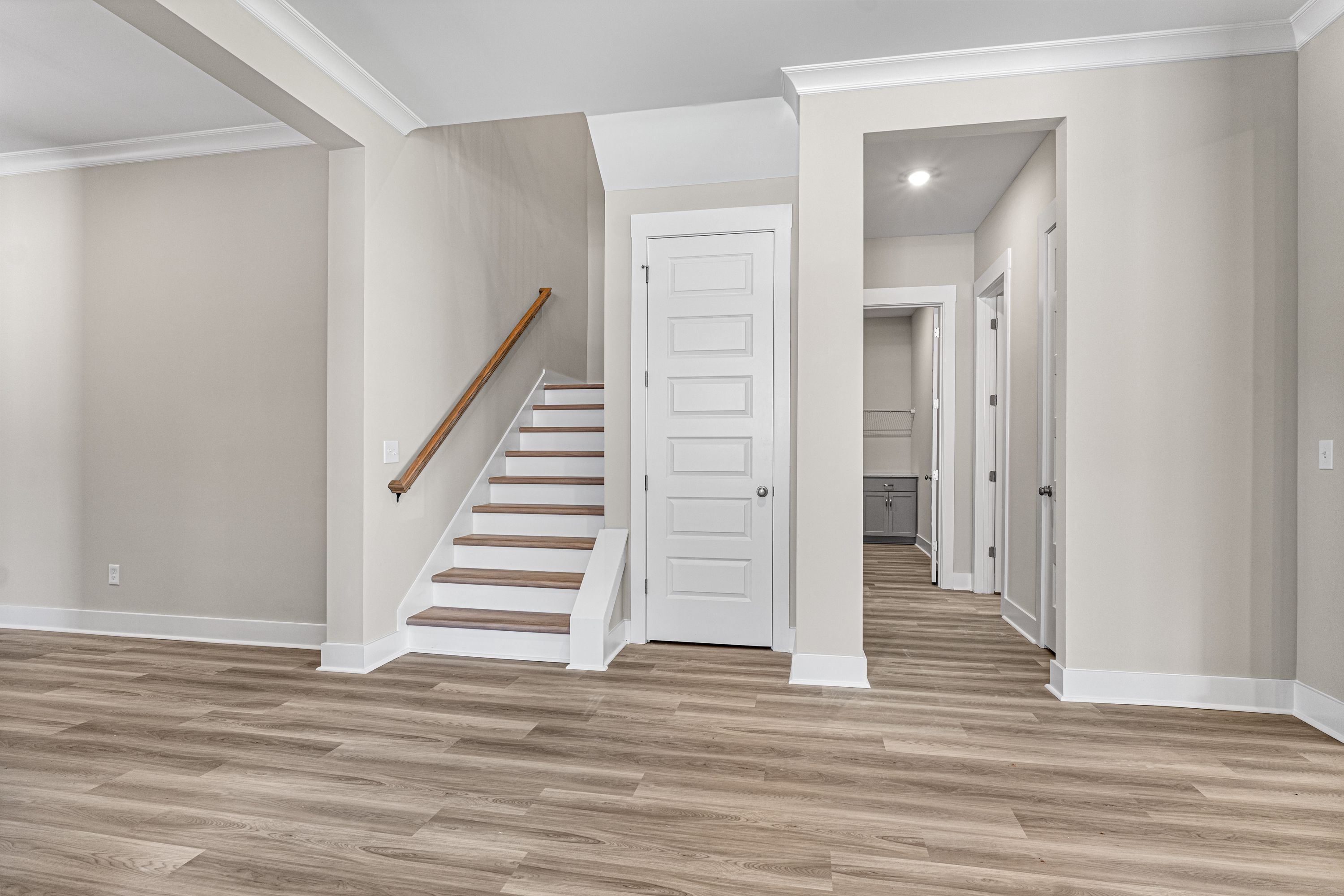 Main floor hallway in The Oxford A with light hardwood floors, wooden staircase, white doors, and powder room access