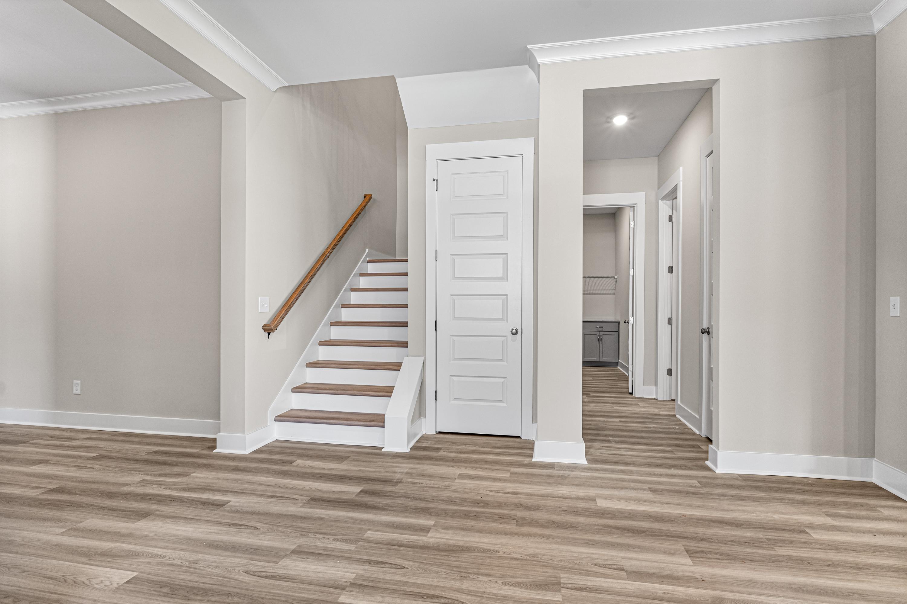 Main floor hallway in The Oxford A with light hardwood floors, wooden staircase, white doors, and powder room access