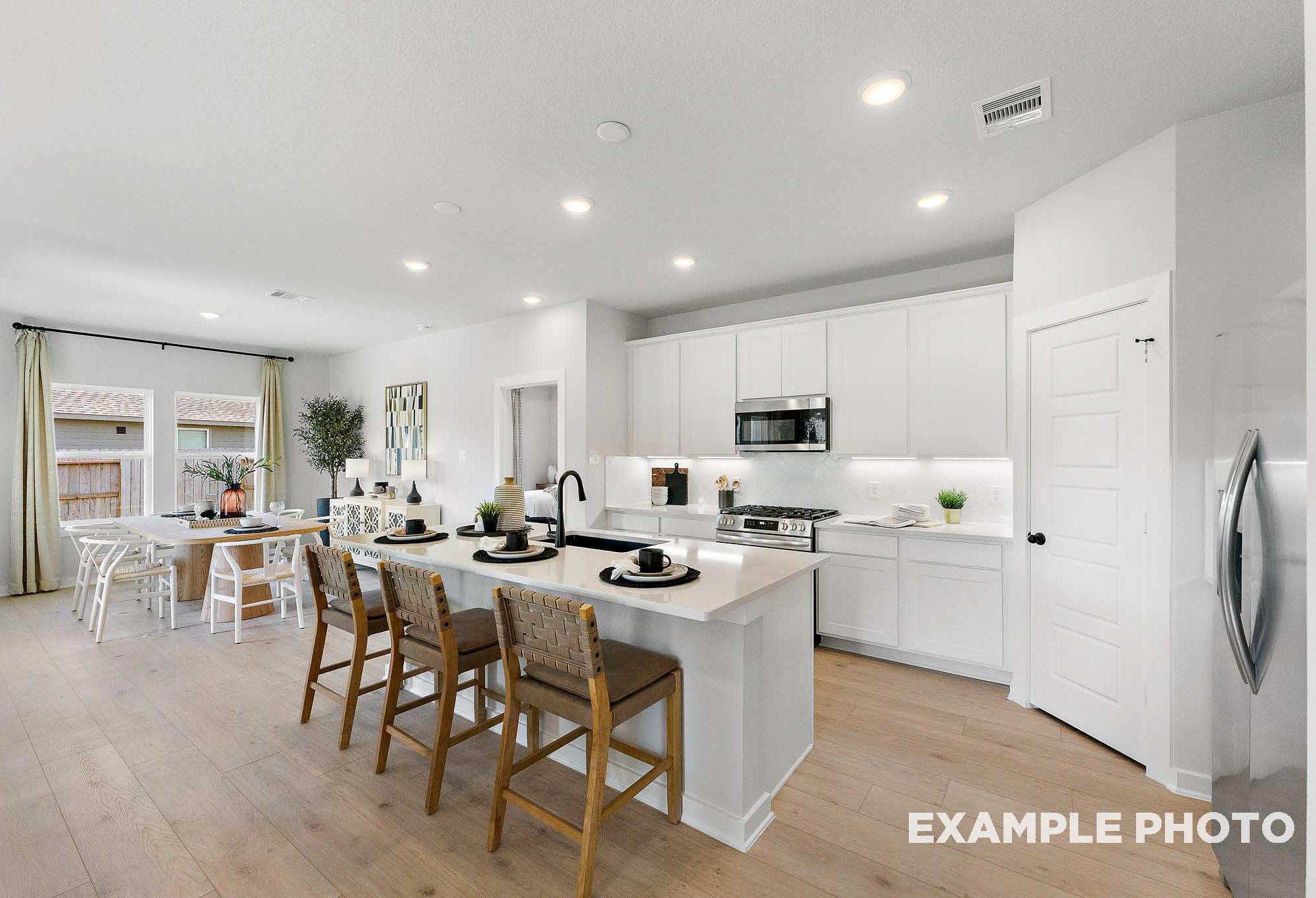 Spacious open-concept kitchen in The Everett C with white shaker cabinets, large island, wood bar stools, and stainless appliances