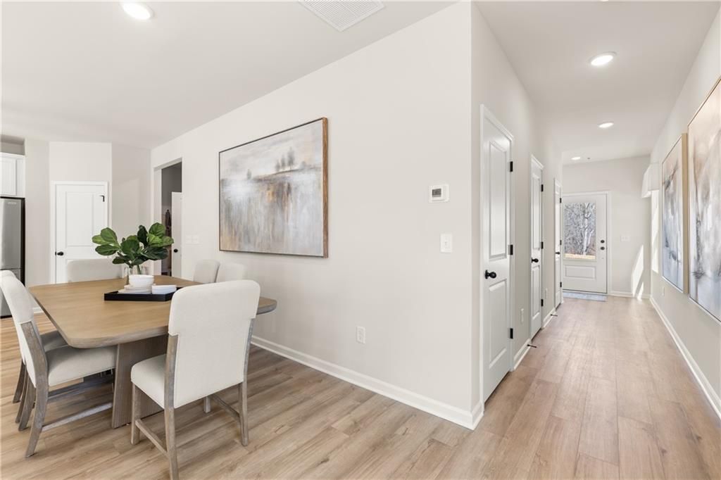 Elegant dining room with wooden table, white chairs, potted plant, abstract art, and open hallway in The Burton C craftsman home, Canton, GA