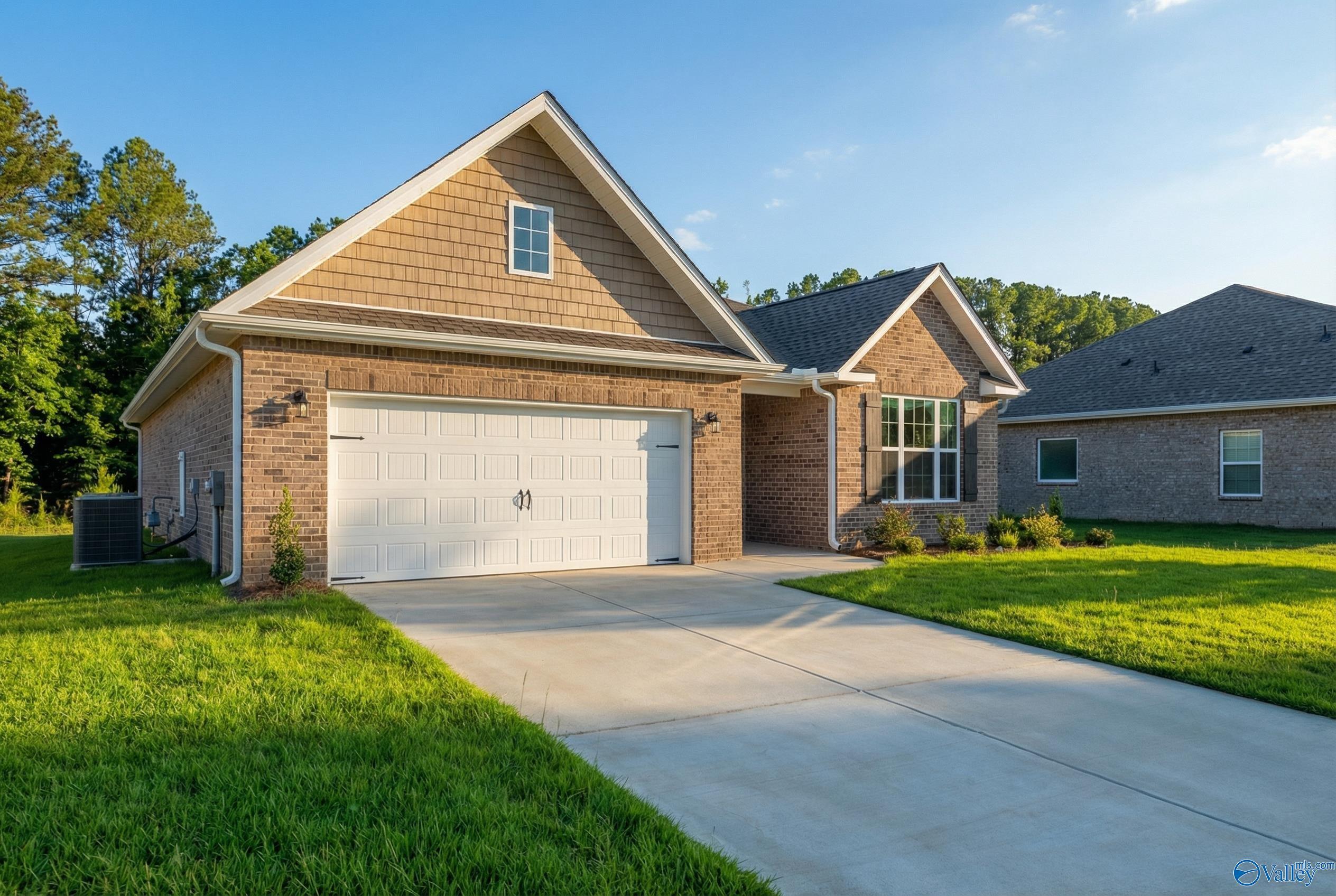 Tan brick 1-story home with 2-car garage, shingled gable roof, driveway, and lush green lawn in Cain Park, Hartselle, Alabama