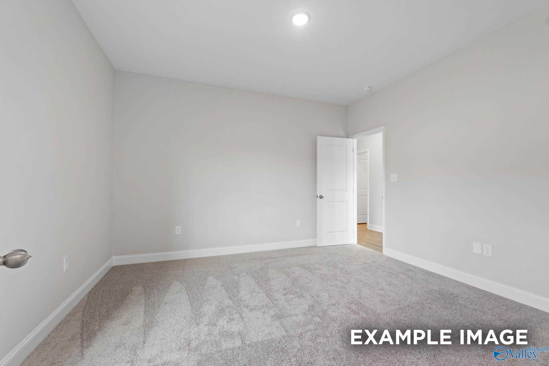Spacious empty bedroom with neutral gray walls, carpet floor, and open door in Davidson Homes The Butler, Jaguar Hills, Huntsville AL