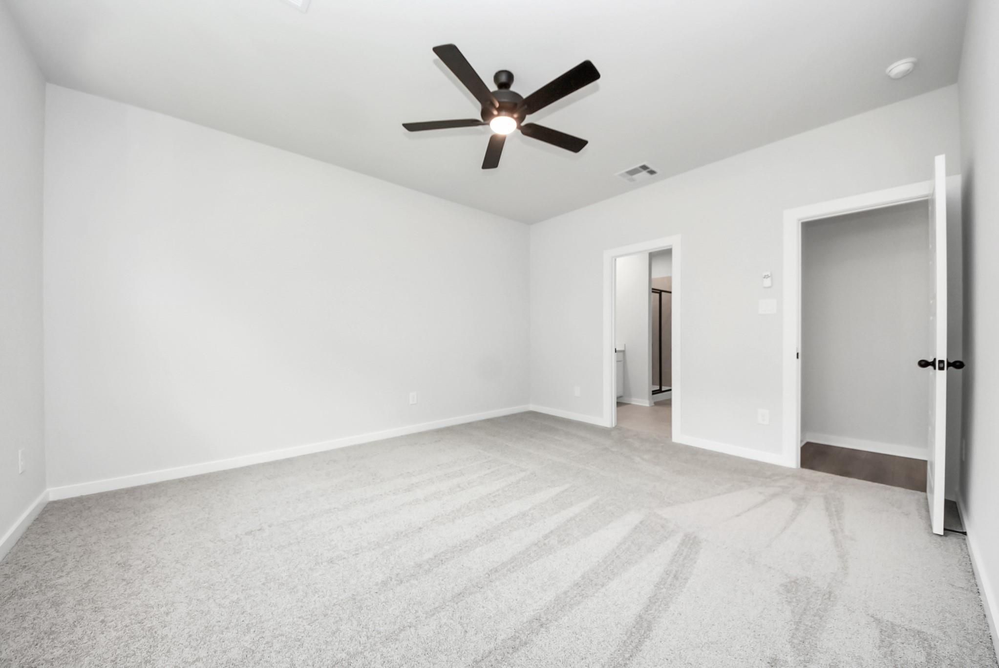 Spacious bedroom with plush carpet and ceiling fan in The Daphne F floor plan by Davidson Homes in Crosby, Texas.