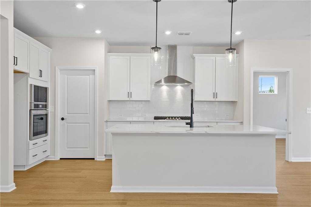 Modern white kitchen featuring large island, stainless steel range hood, subway tile backsplash in Davidson Homes The Edison A, Loganville GA