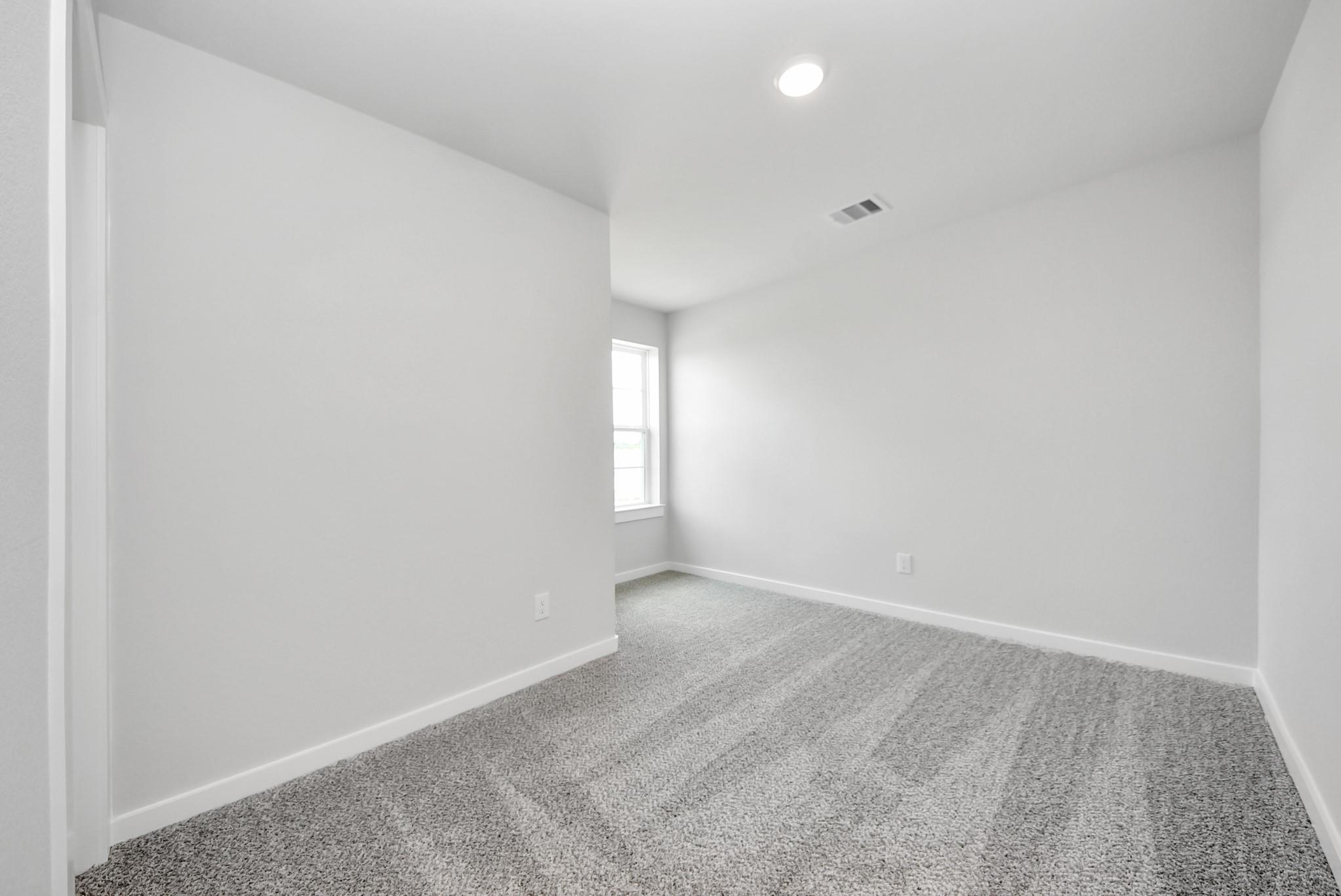 Bright, carpeted bedroom with neutral walls in The Sabine E floor plan at Windmill Estates, Magnolia, Texas.