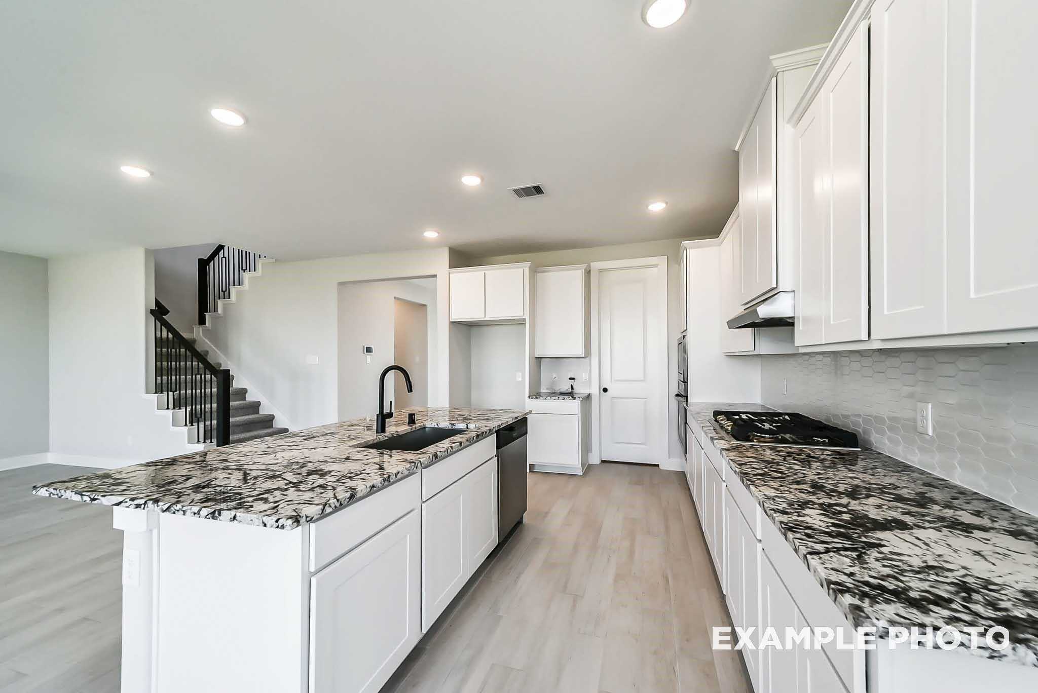 Modern white kitchen with speckled granite island, gas cooktop, stainless appliances in Davidson Homes The Philip C, Rosharon TX