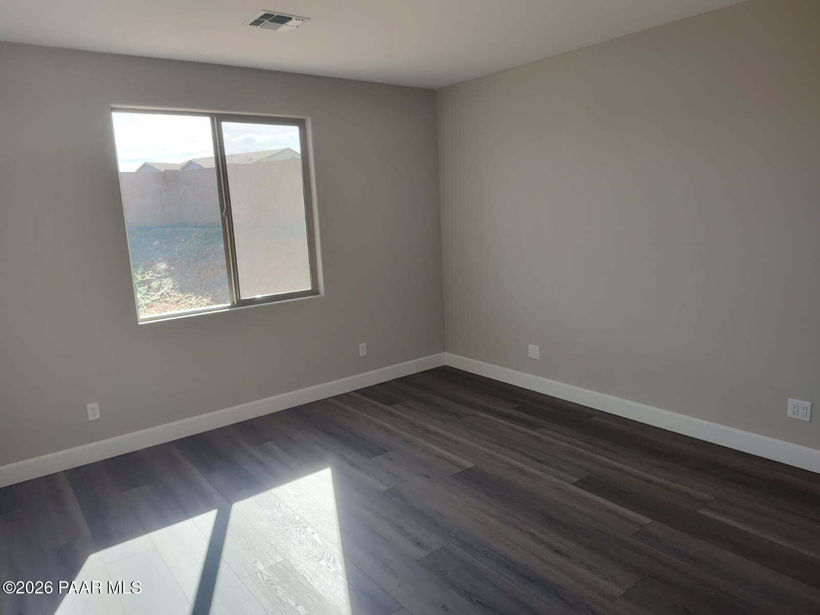 Empty bedroom featuring light gray walls, gray luxury vinyl plank flooring, and large sliding window with desert view in Davidson Homes The Harmony C, Prescott Valley, Arizona