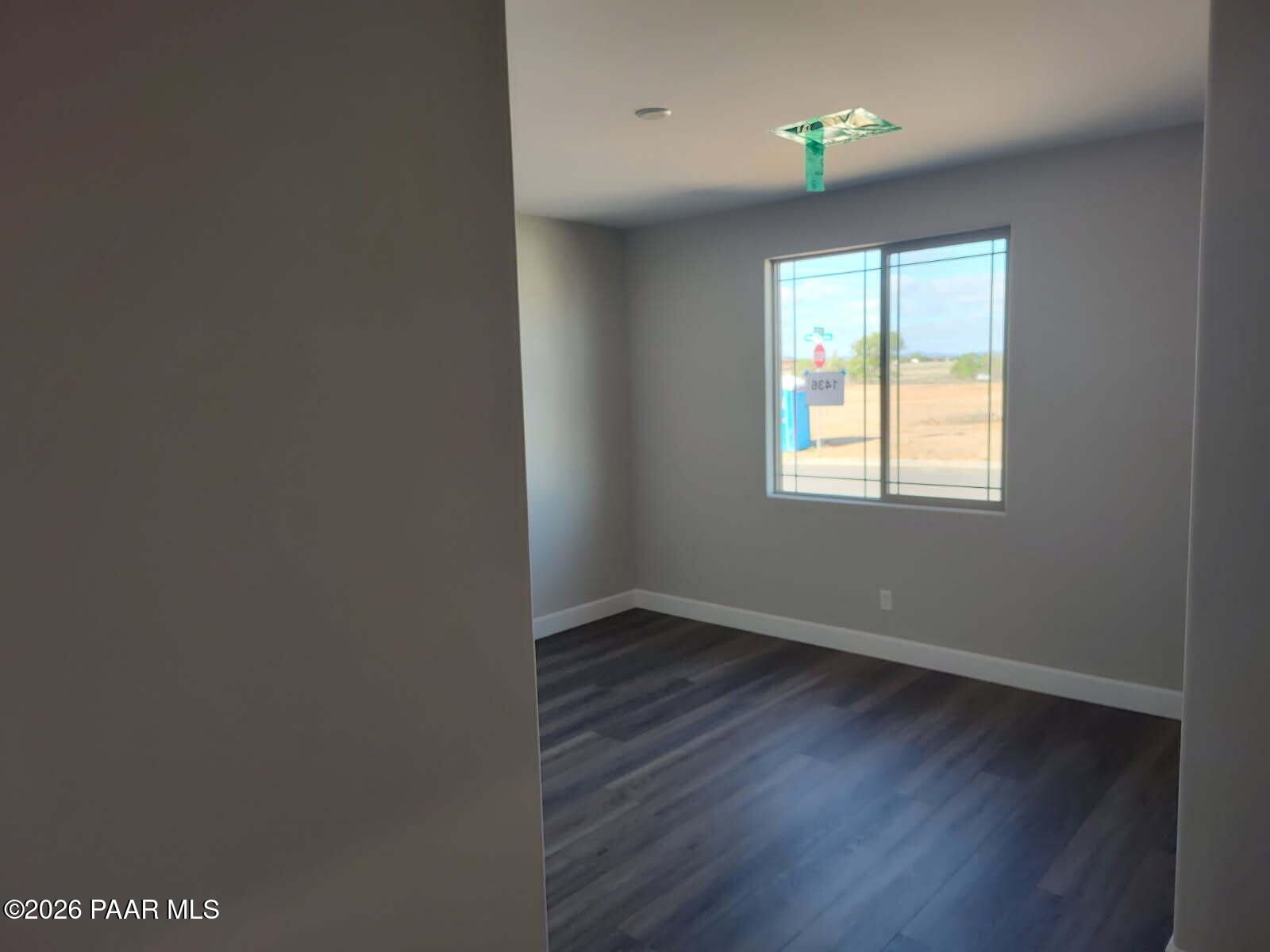 Empty bedroom with gray walls, luxury vinyl plank flooring, and large window overlooking arid construction site in Davidson Homes Harmony C, Prescott Valley, AZ