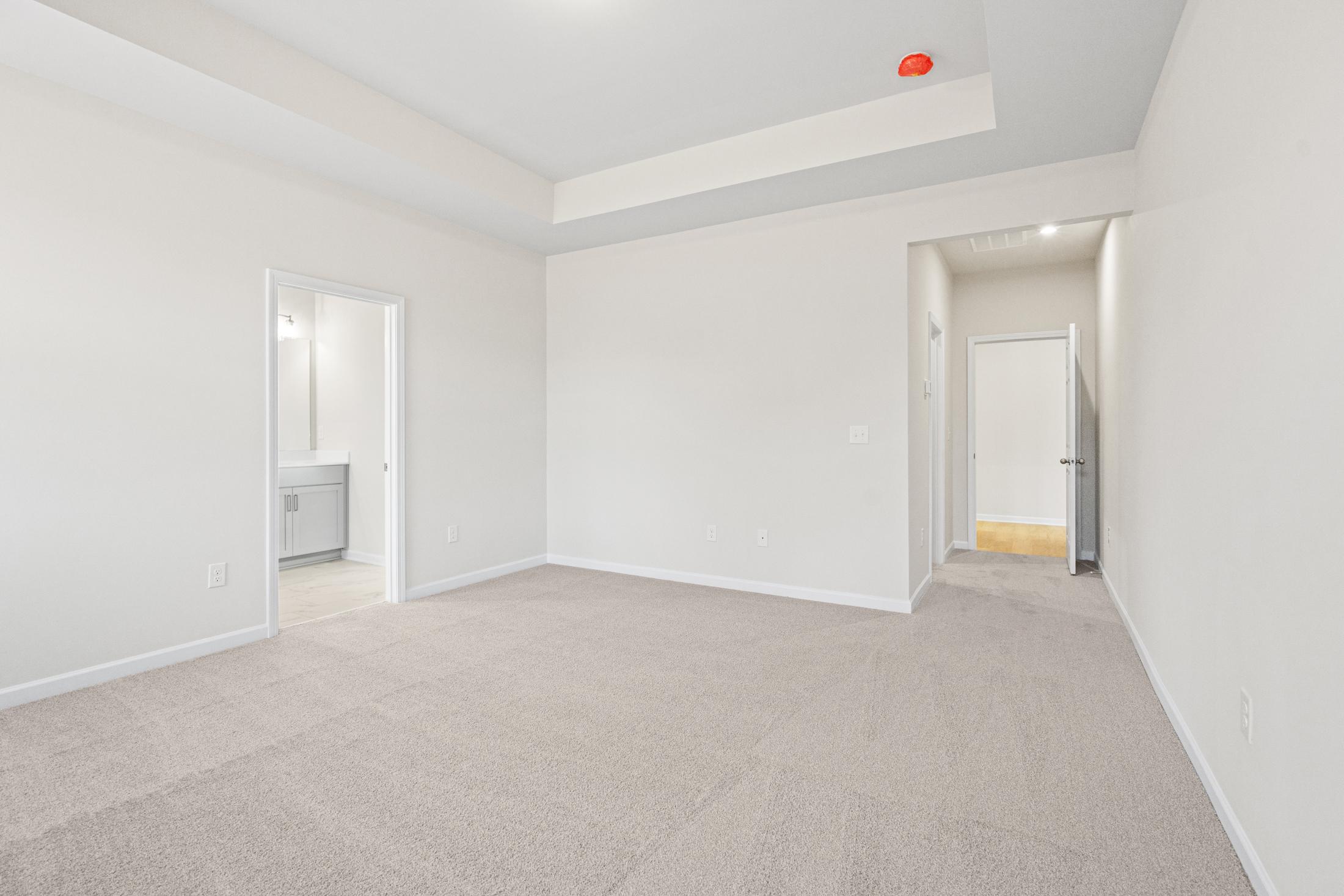 Spacious master bedroom in The Glenwood A featuring tray ceiling, neutral carpet, and en-suite bathroom with vanity