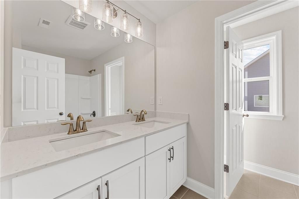 Elegant master bathroom double vanity with white quartz counters, gold faucets, and chandelier in Davidson Homes The Willow B, Hoschton, GA