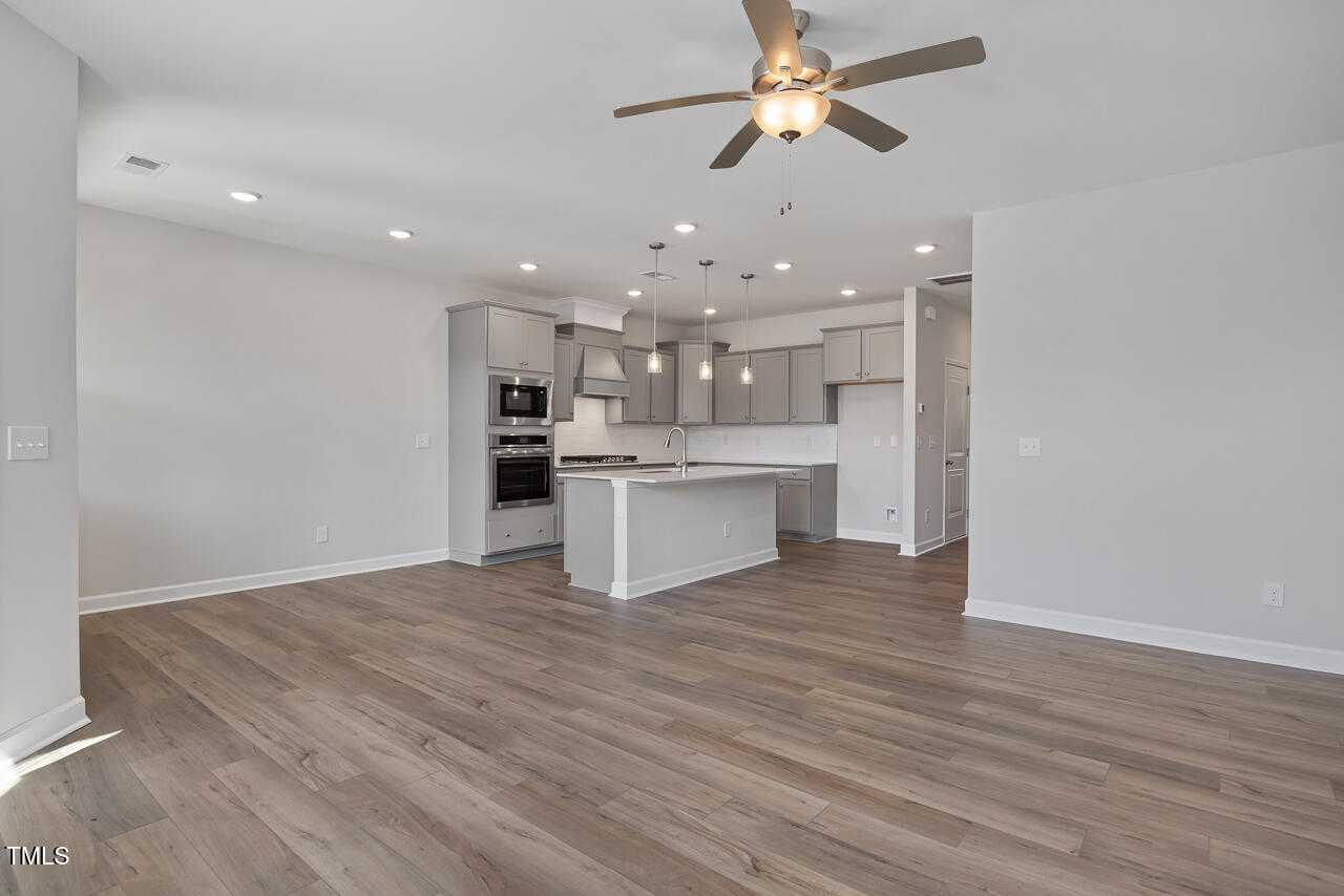 Spacious modern kitchen with white cabinets, quartz island, stainless double oven, pendant lights, ceiling fan in Davidson Homes The Graham, Fuquay-Varina, NC