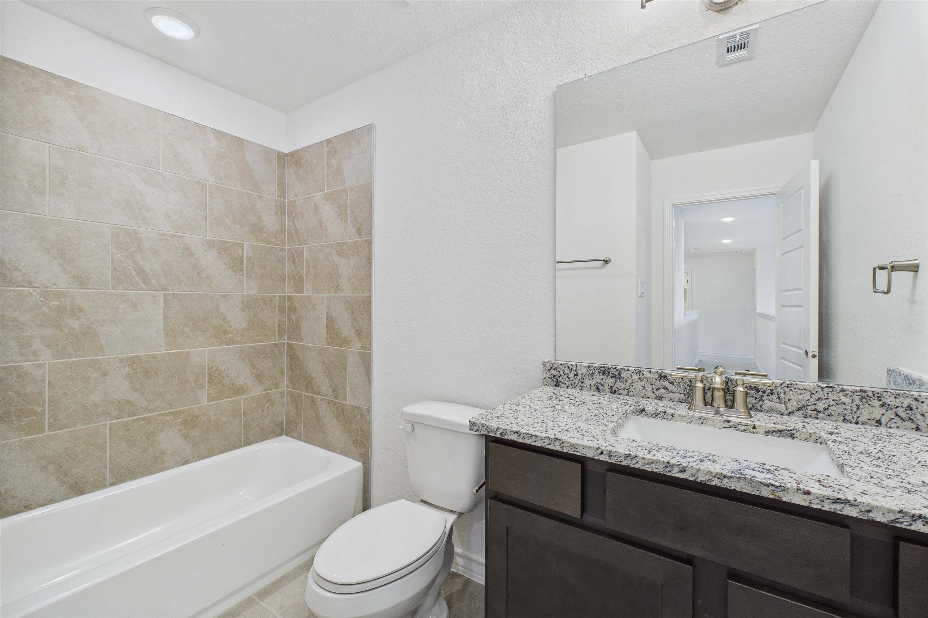 Modern bathroom in The Danbury with granite vanity, dark cabinets, and tiled shower surround in Castroville, Texas home.
