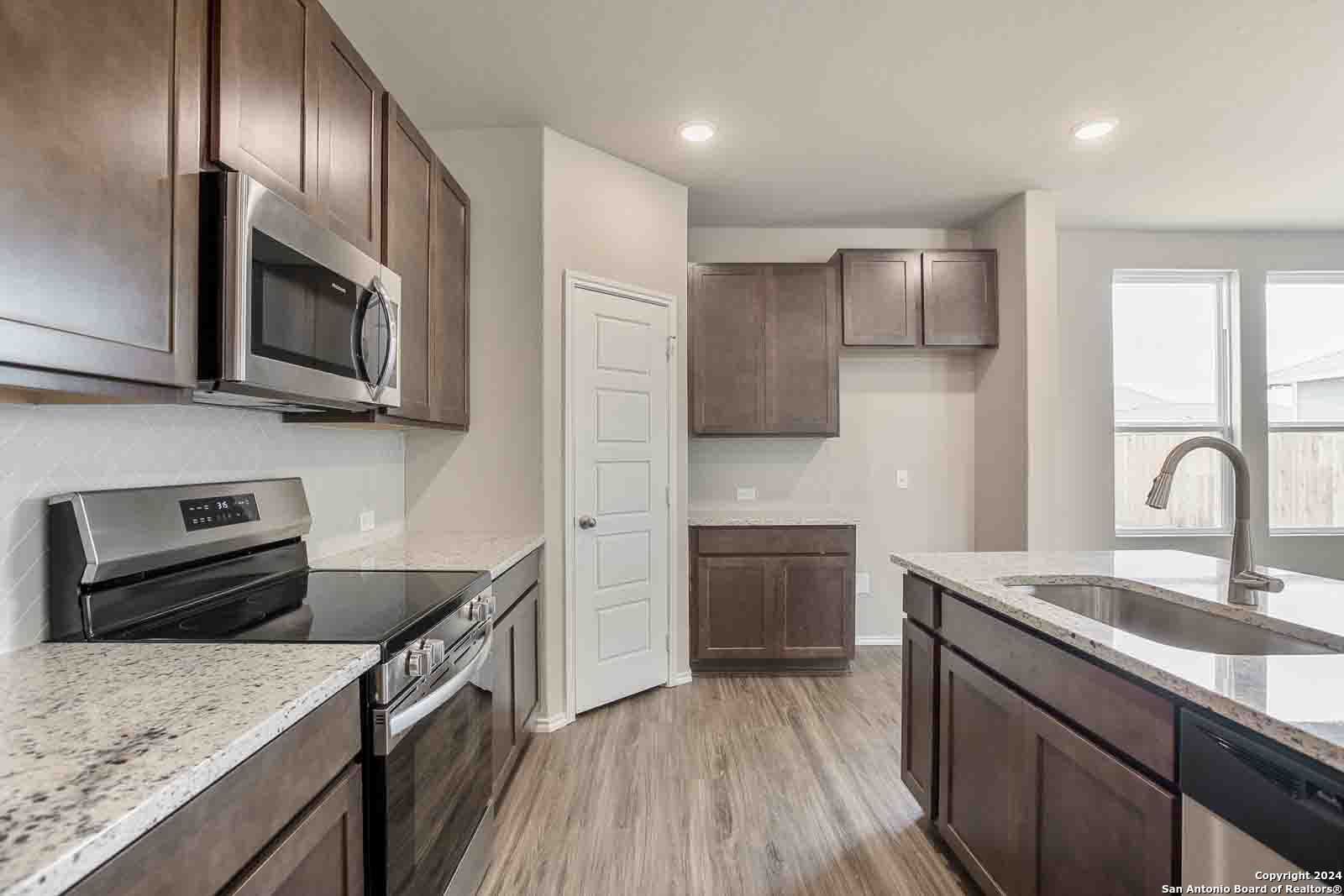 Modern kitchen featuring dark wood cabinets, granite island sink, stainless steel appliances in Davidson Homes The Murray H, Seguin, Texas