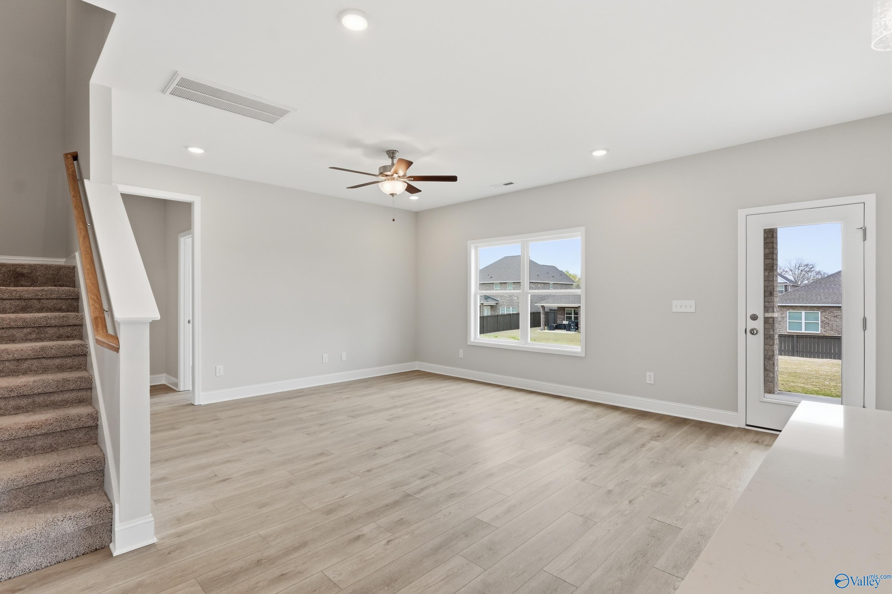Bright living room with hardwood floors, white staircase, ceiling fan, and large windows to backyard in Davidson Homes The Shelby B, New Market, Alabama