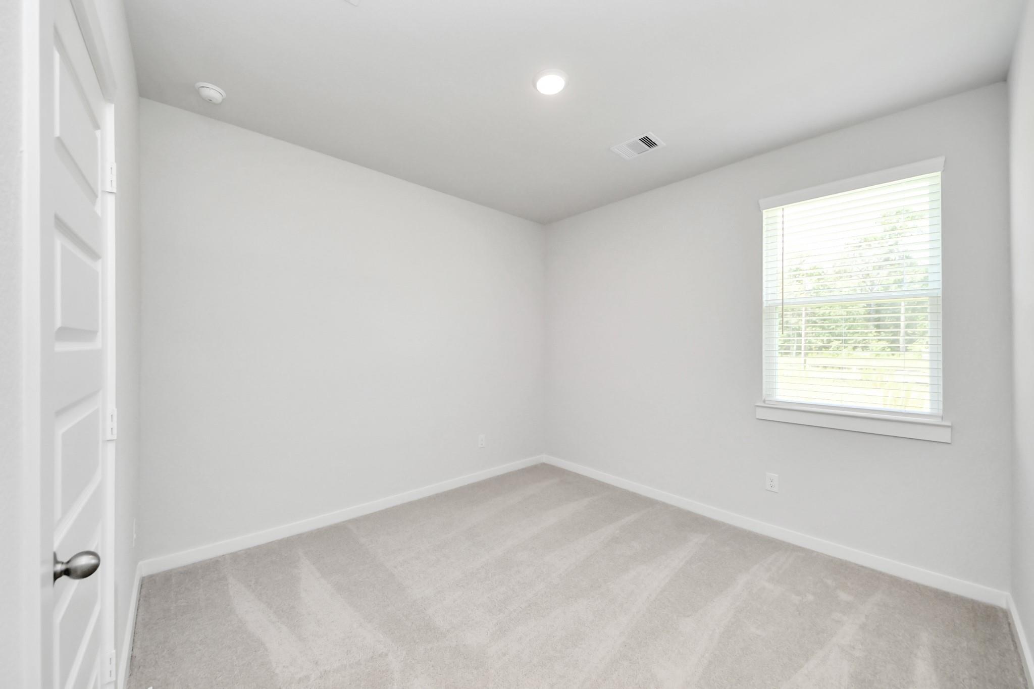 Bright, empty secondary bedroom with neutral carpet and window blinds in The Frio F plan at Liberty Estates, Cleveland.