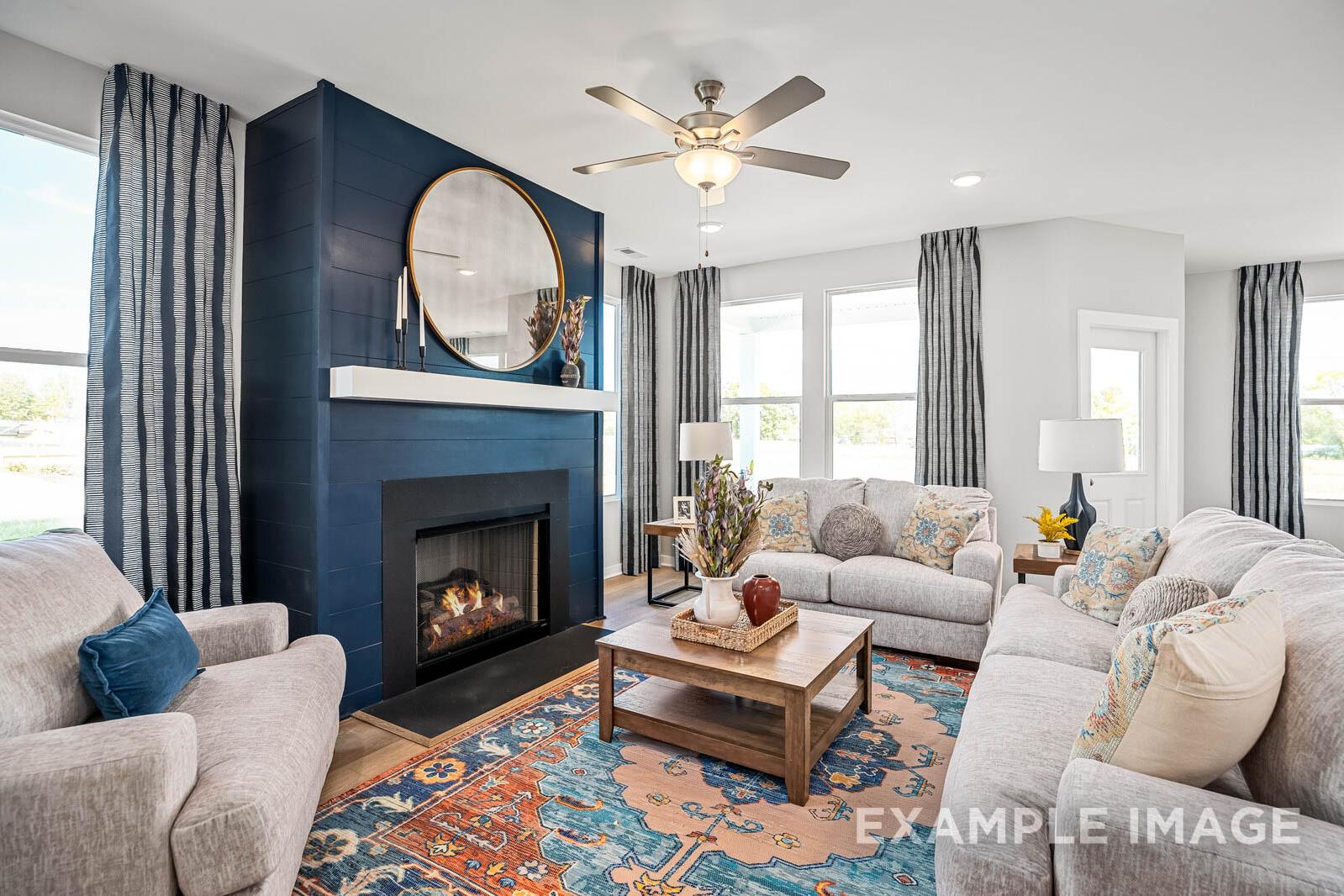 Cozy living room in The Franklin B featuring navy blue fireplace wall, round mirror, beige sofas, wooden coffee table, and area rug
