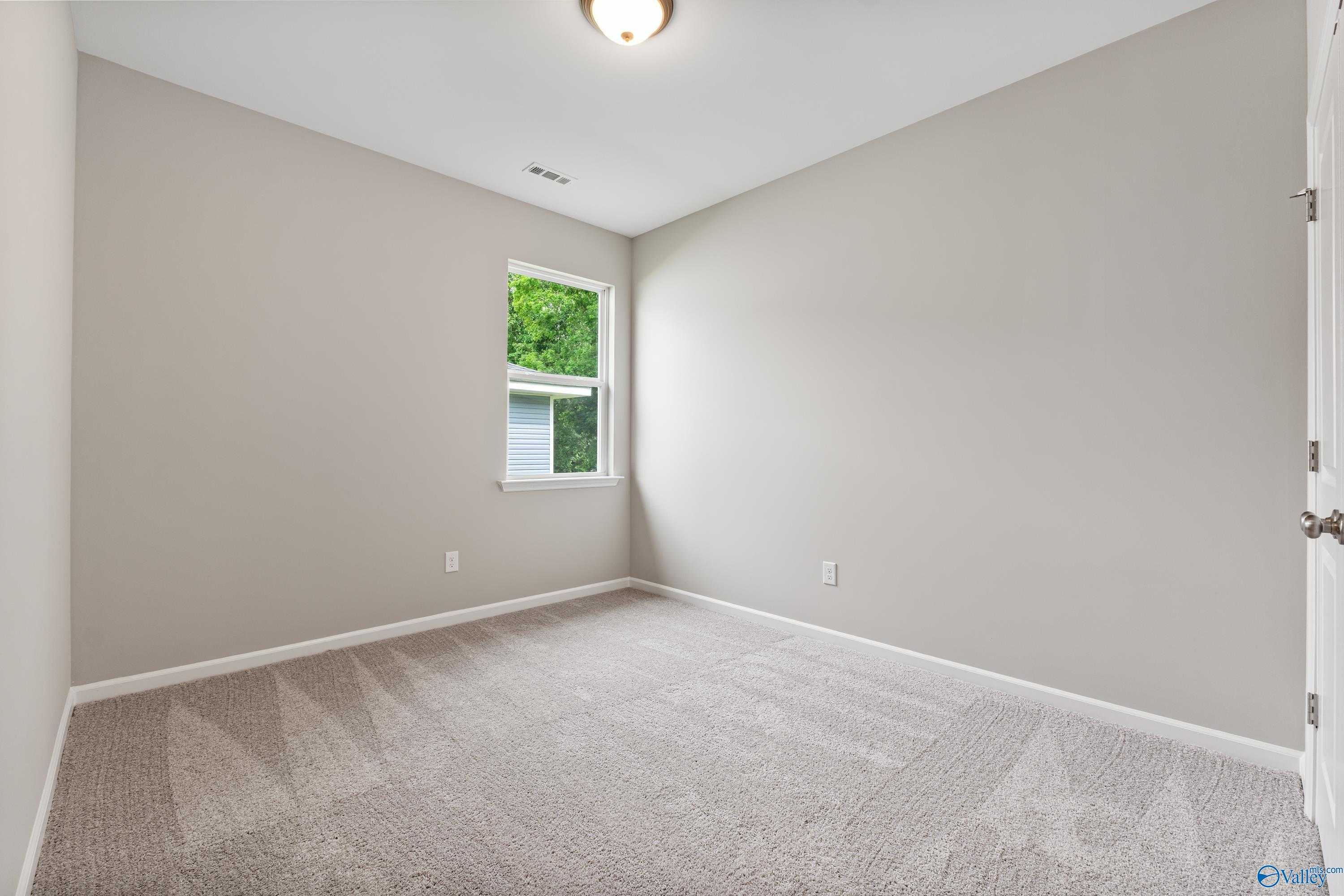 Bright secondary bedroom with light gray walls, plush carpet, and window overlooking greenery in Davidson Homes The Aurora, Fayetteville