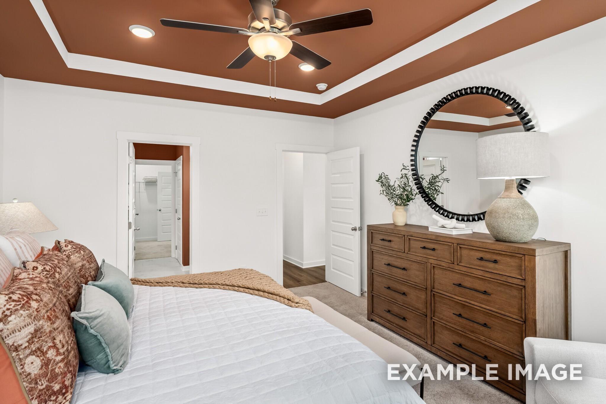 Elegant master bedroom with tray ceiling, ceiling fan, king bed, round mirror, and en-suite bath in Davidson Homes The Ash A, Gallatin, TN